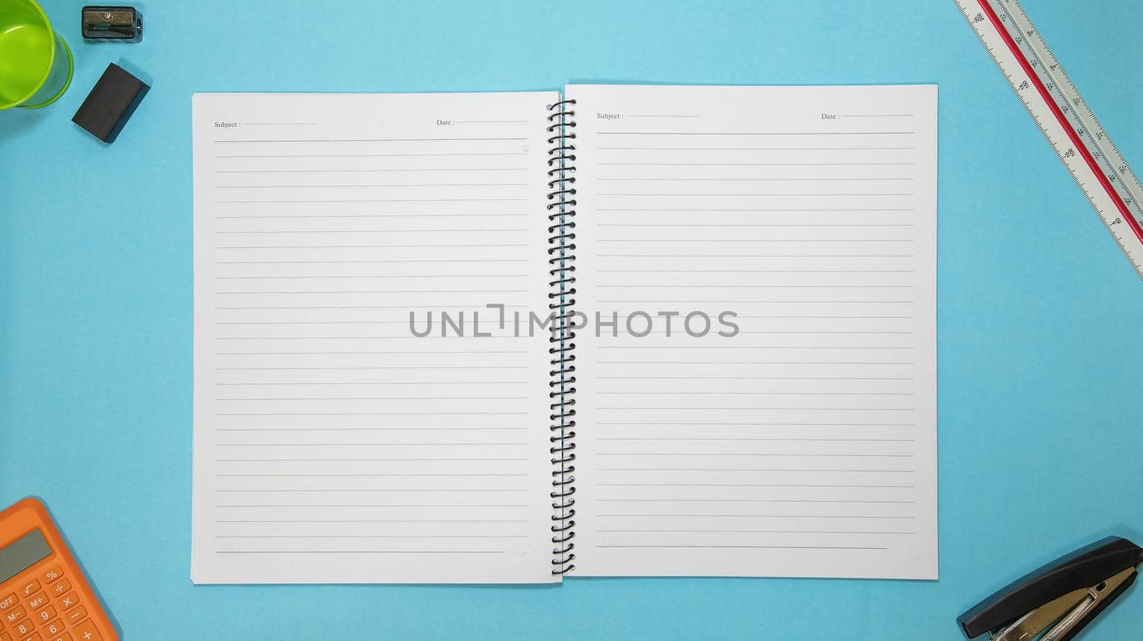 Office table desk with set of colorful supplies, blue blank note pad, cup, pen, pc, crumpled paper, flower on blue background. Top view and copy space for text