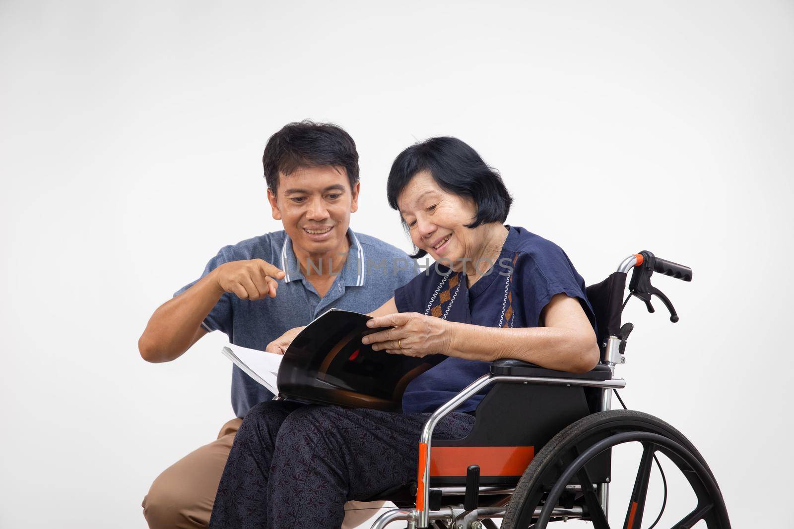 Elderly woman reading a book on wheelchair with her son take care.