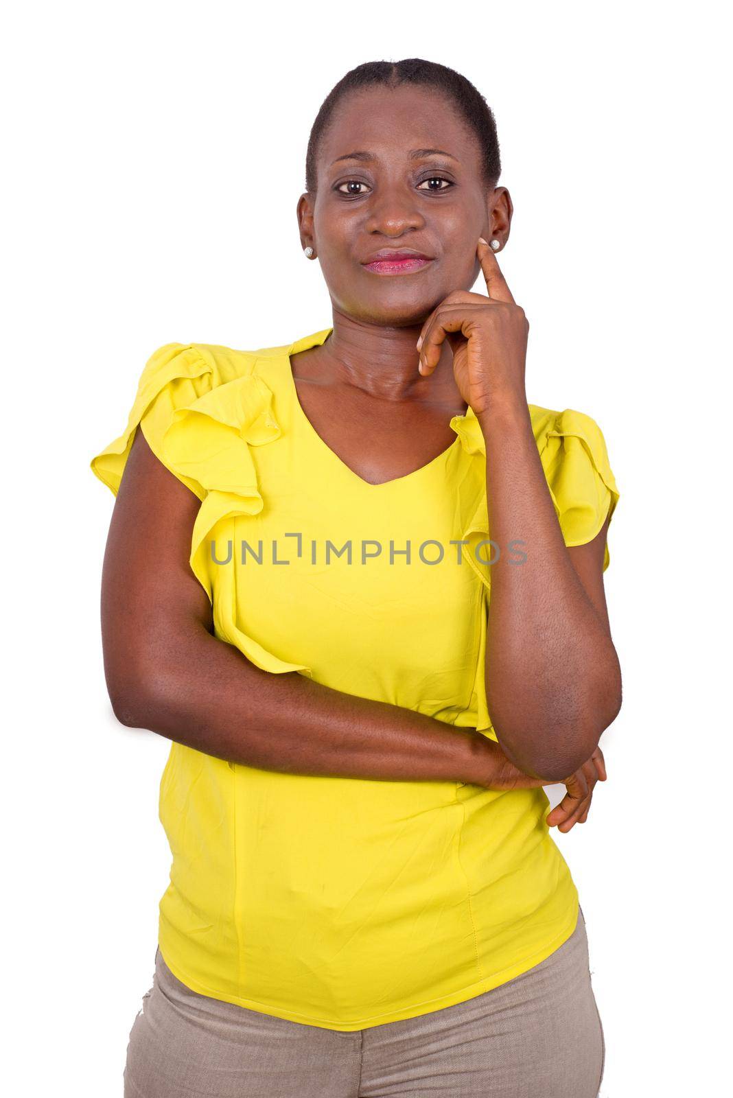 African girl in yellow camisole standing on gray background with hand under chin and smiles at the camera.