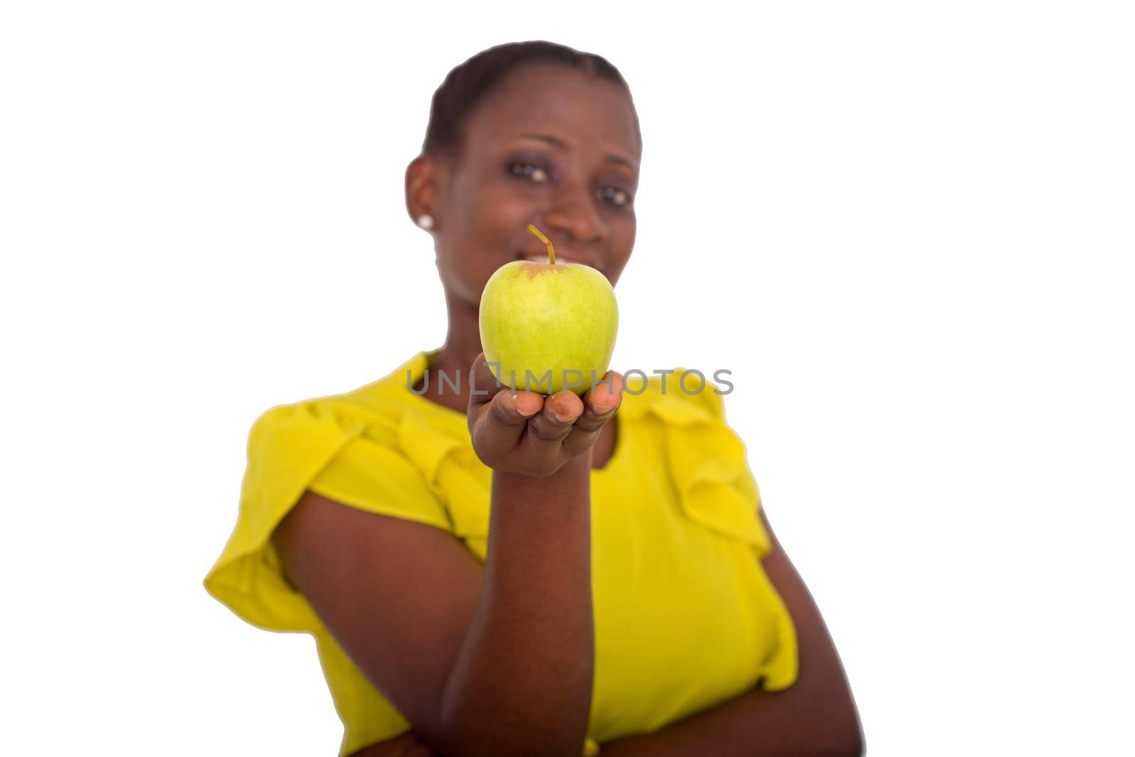 young girl standing in yellow camisole showing an apple smiling at the camera.
