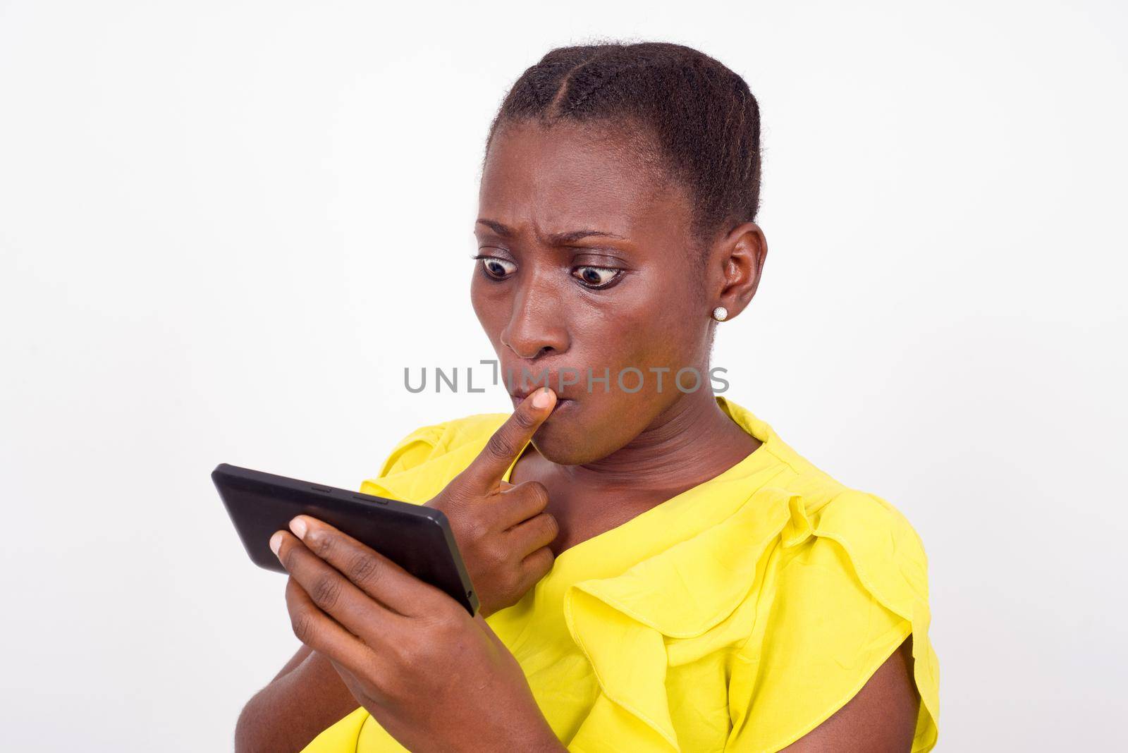 young girl standing in yellow camisole looks at her mobile phone, surprised.