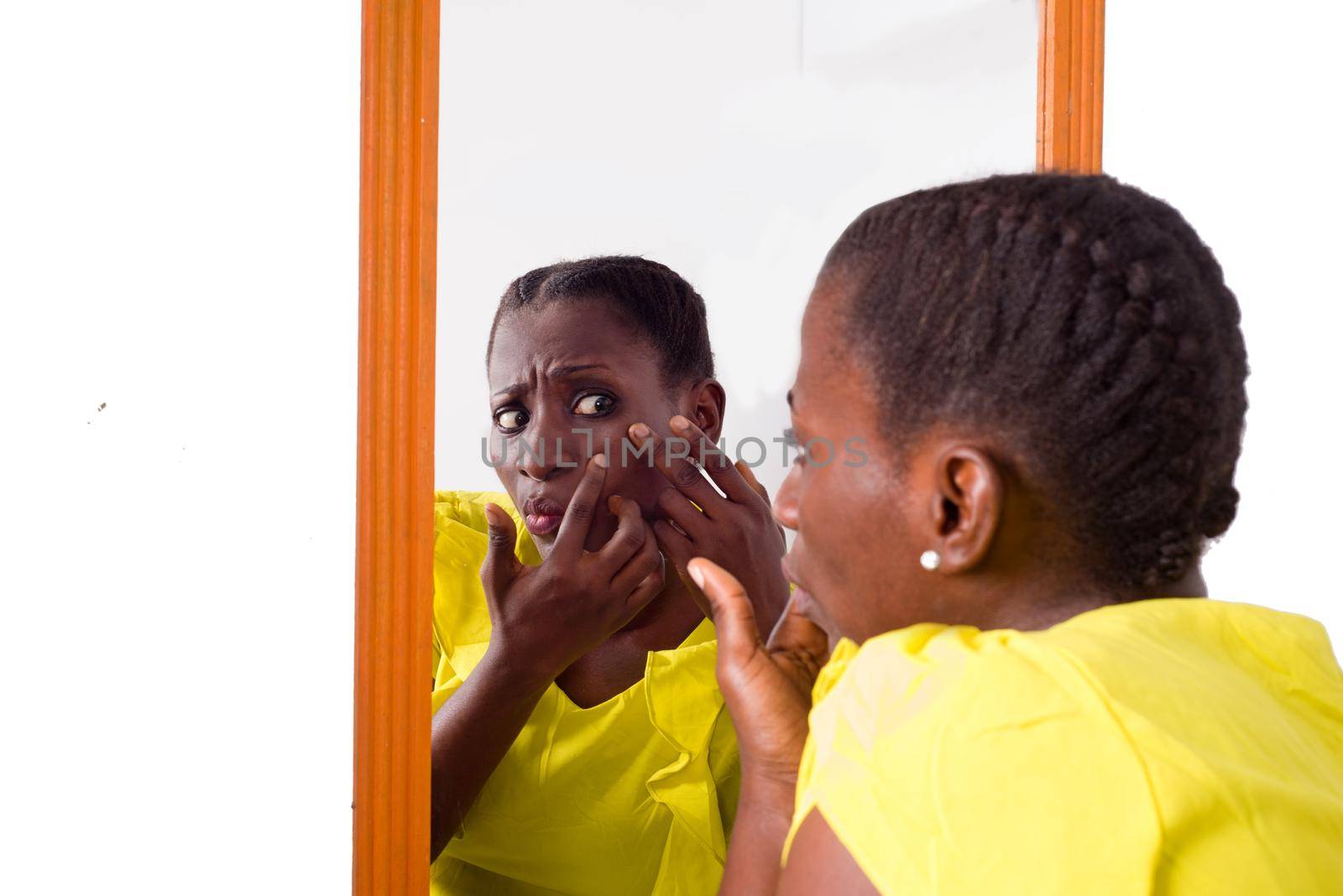 African girl standing in yellow camisole looking at herself in a mirror.