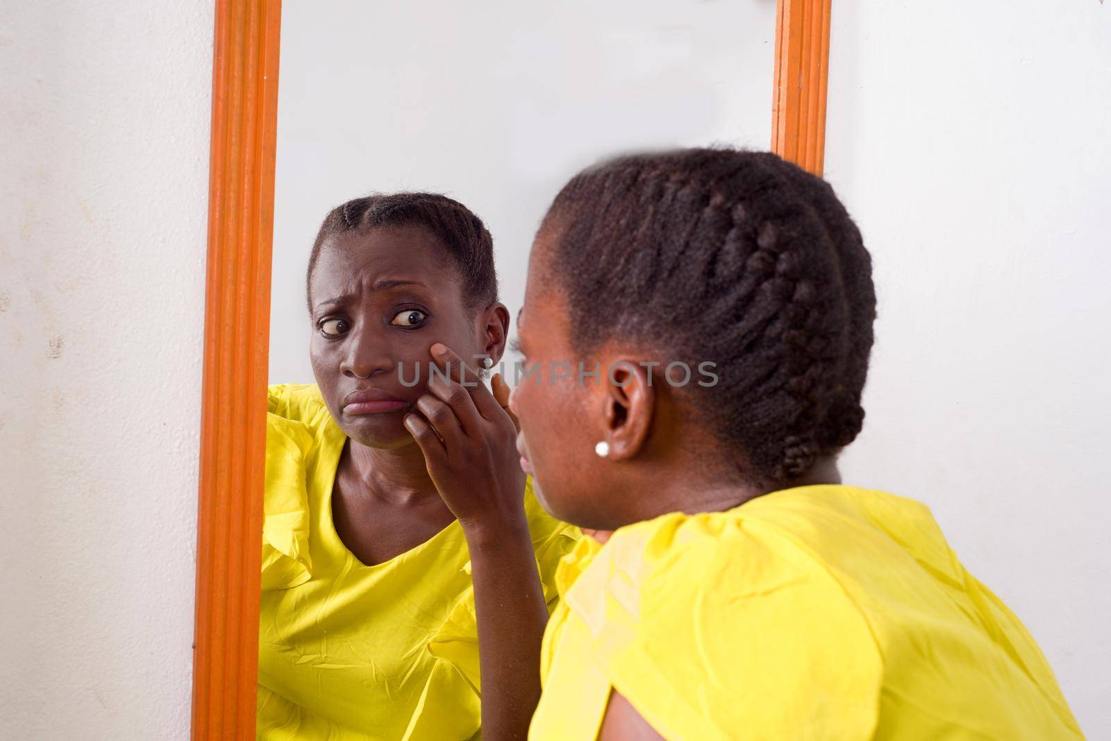 African girl standing in yellow camisole looking at herself in a mirror.