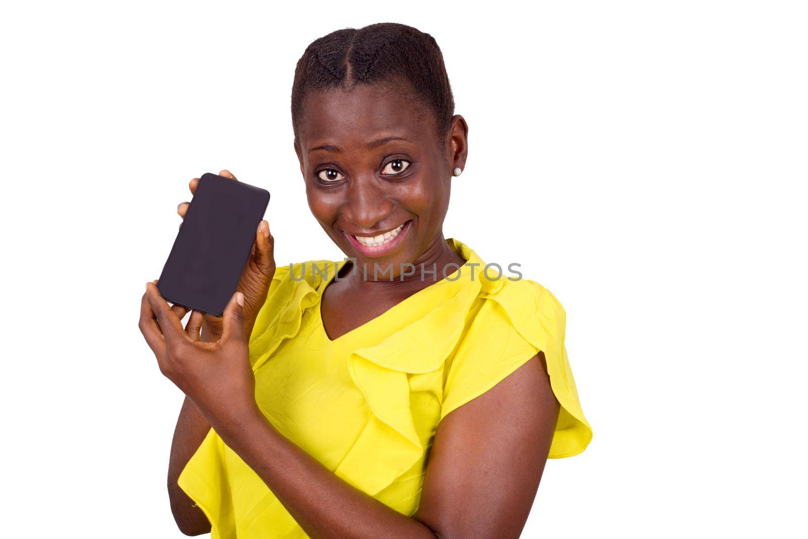young girl standing in yellow camisole shows her mobile phone while smiling at the camera.