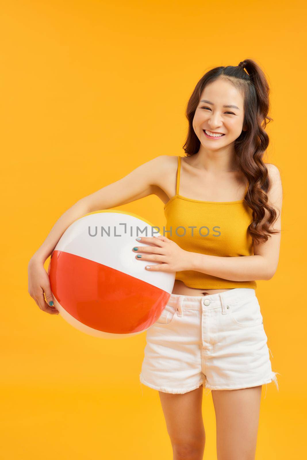 Happy young Asian woman holding beach ball in summer holiday travel on orange background. by makidotvn