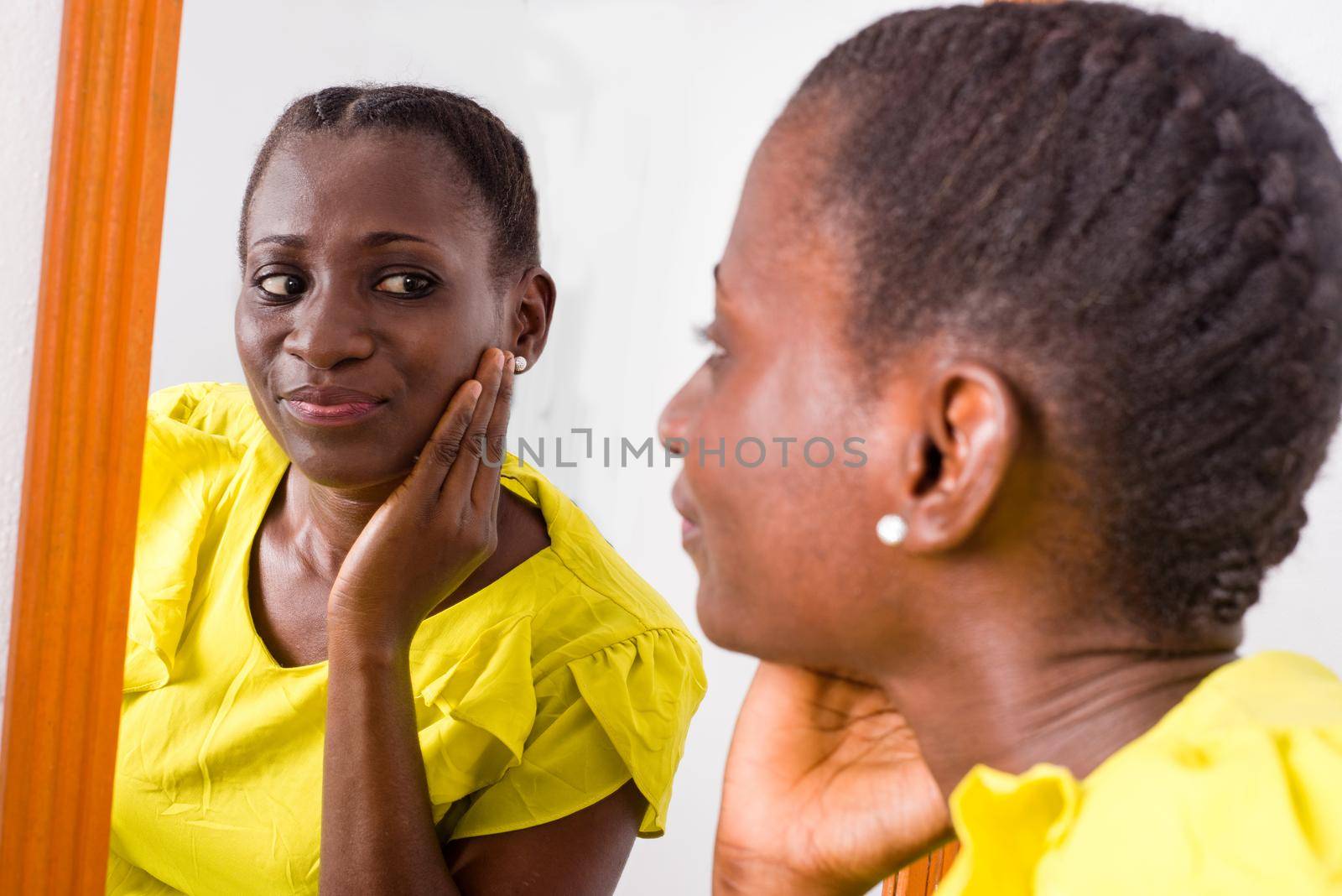 African girl standing in yellow tank looking at herself in a mirror smiling.