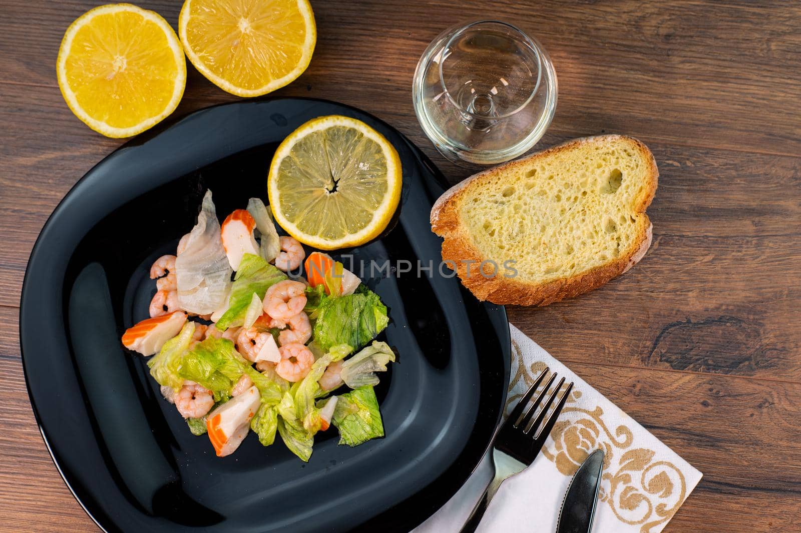 composition of a black plate with shrimp and surimi salad on wooden background