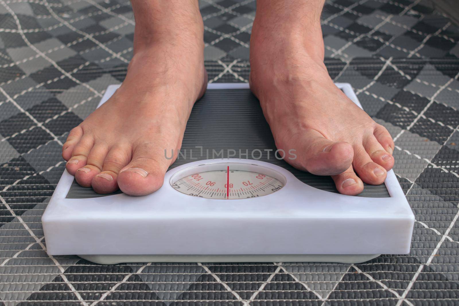 A young man is weighed barefoot on the scales in order to control his weight, keep a diet and lead a healthy lifestyle