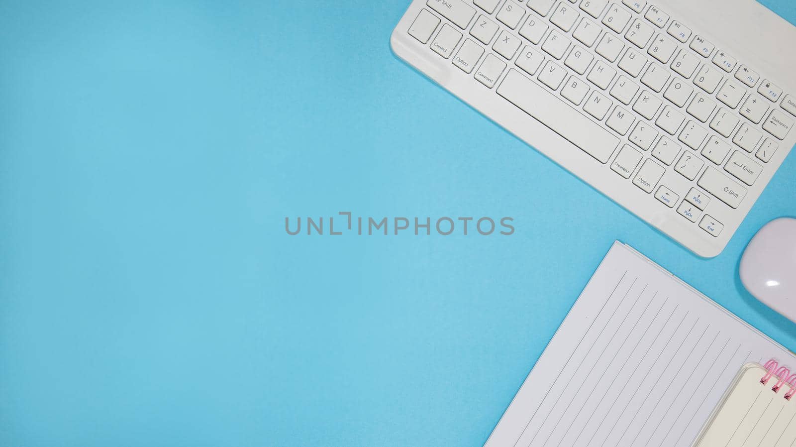 Office table desk with set of colorful supplies, blue blank note pad, cup, pen, pc, crumpled paper, flower on blue background. Top view and copy space for text