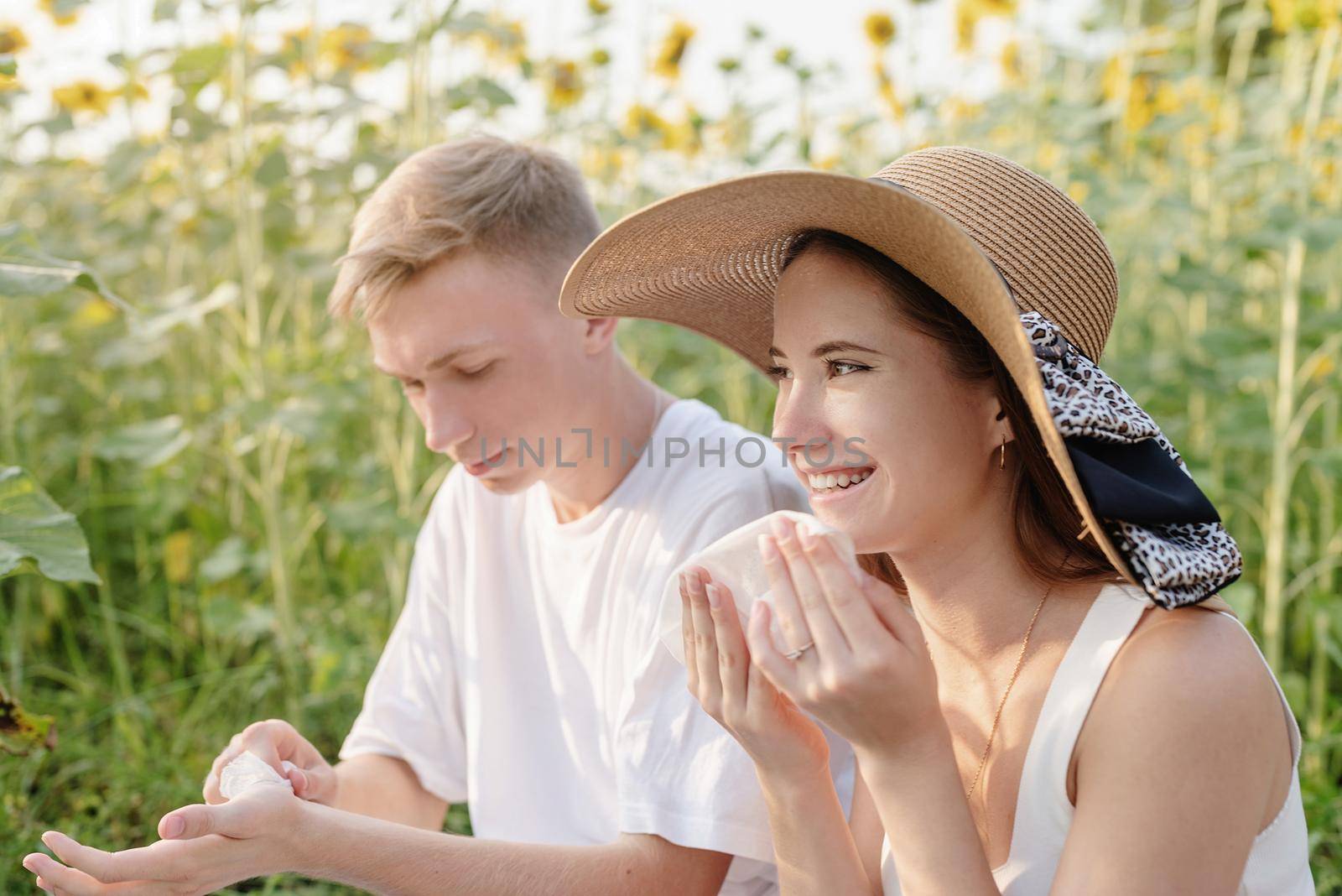 Autumn nature. Fun and liesure. Young teenage couple having picnic on sunflower field in sunset, having fun looking away, wiping their hands and faces