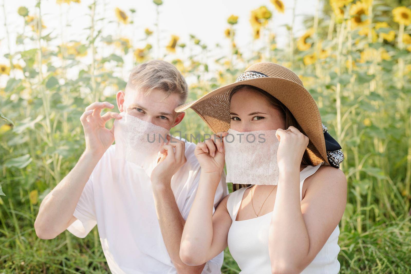 Young couple having picnic on sunflower field at sunset, making funny faces by Desperada