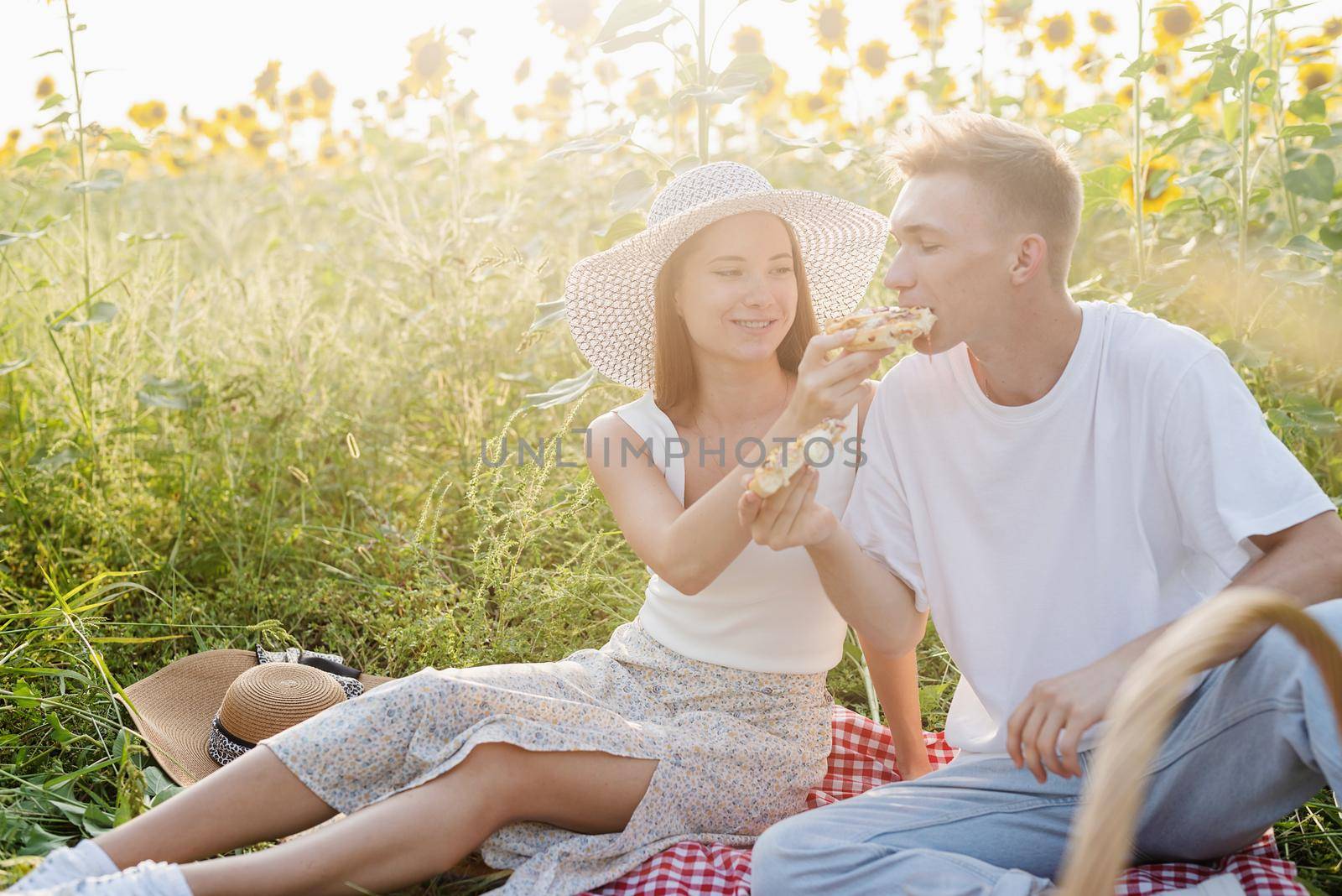 Young couple having picnic on sunflower field at sunset by Desperada