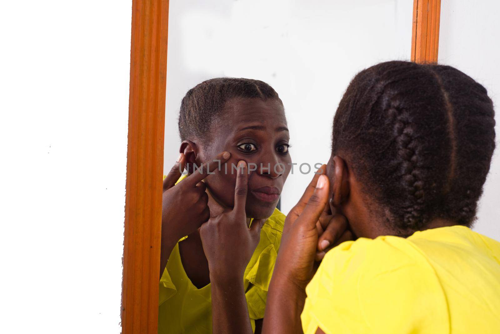 African girl standing in yellow camisole looking at herself in a mirror.