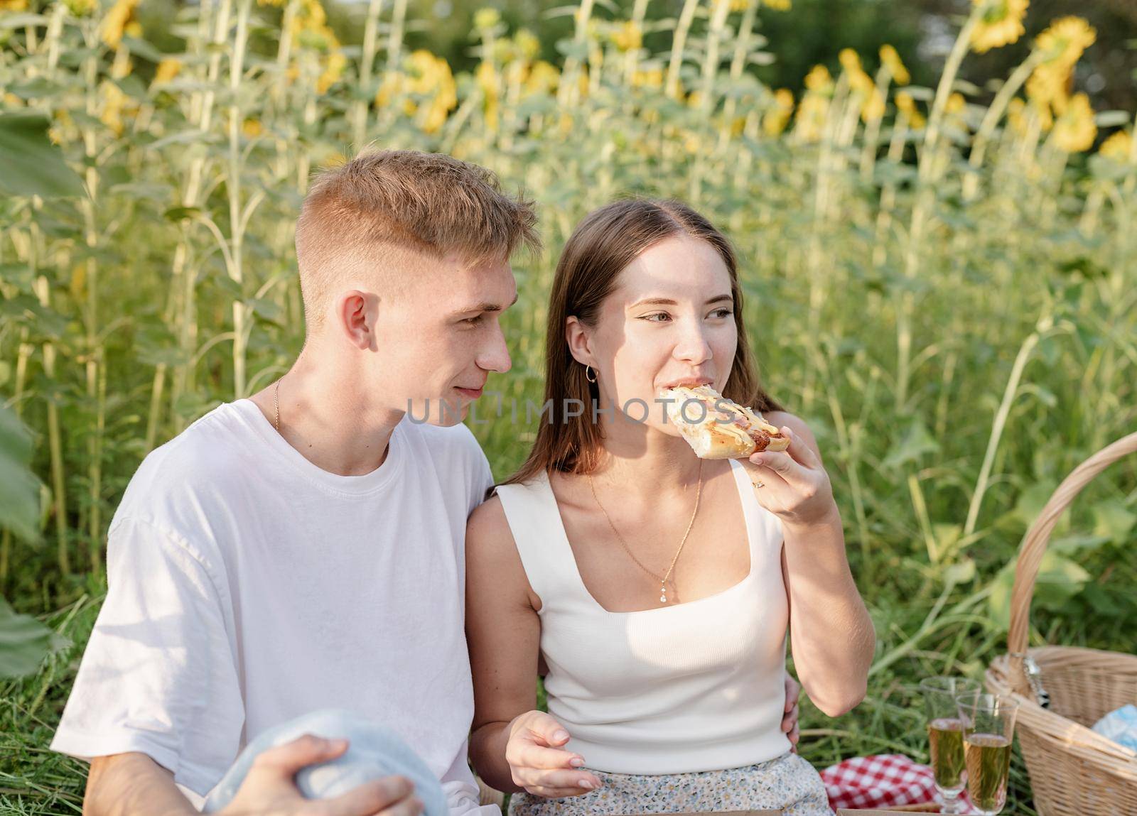 Young couple having picnic on sunflower field at sunset by Desperada