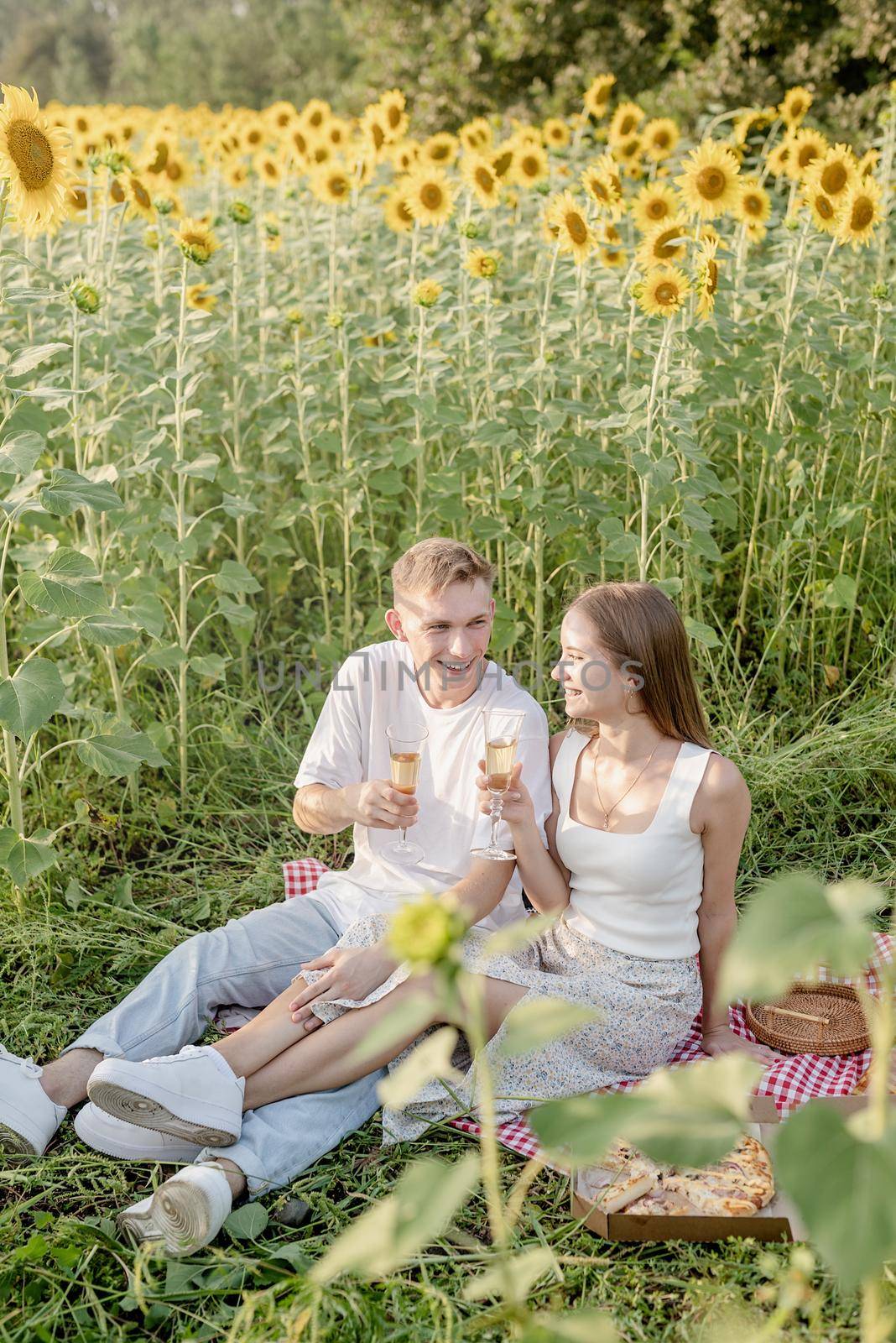 Autumn nature. Fun and liesure. Young teenage couple picnic on sunflower field in sunset drinking champagne