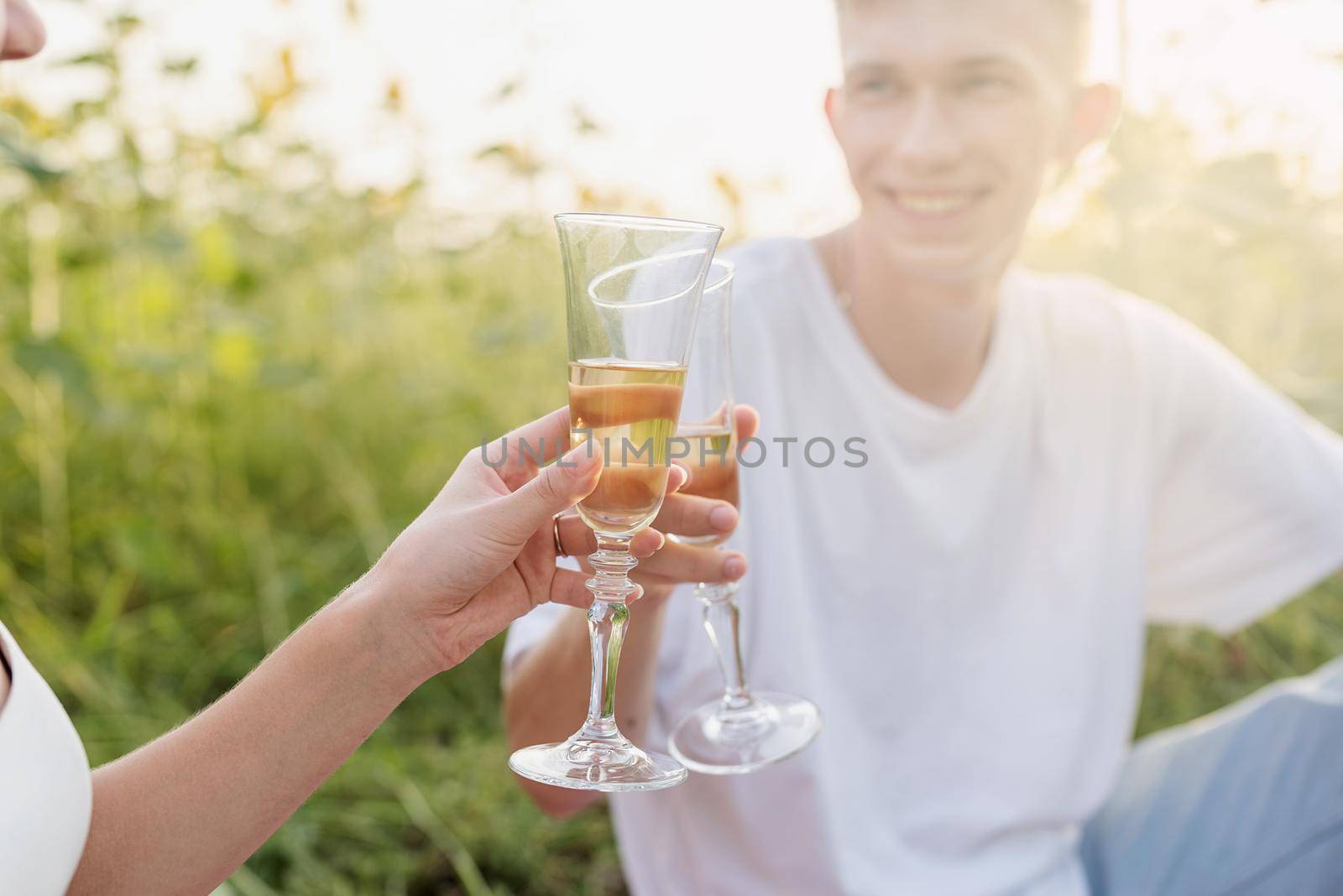 Autumn nature. Fun and liesure. Young teenage couple picnic on sunflower field in sunset drinking champagne toasting