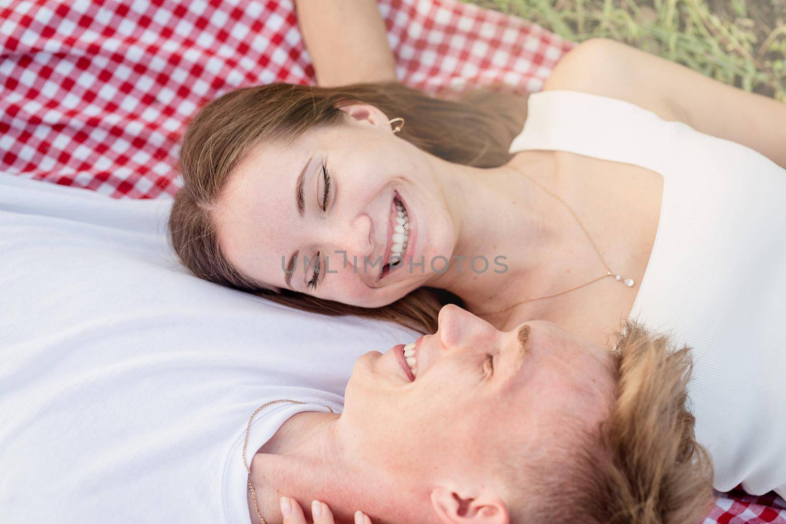 Young happy romantic couple cuddling on a picnic blanket looking to each other