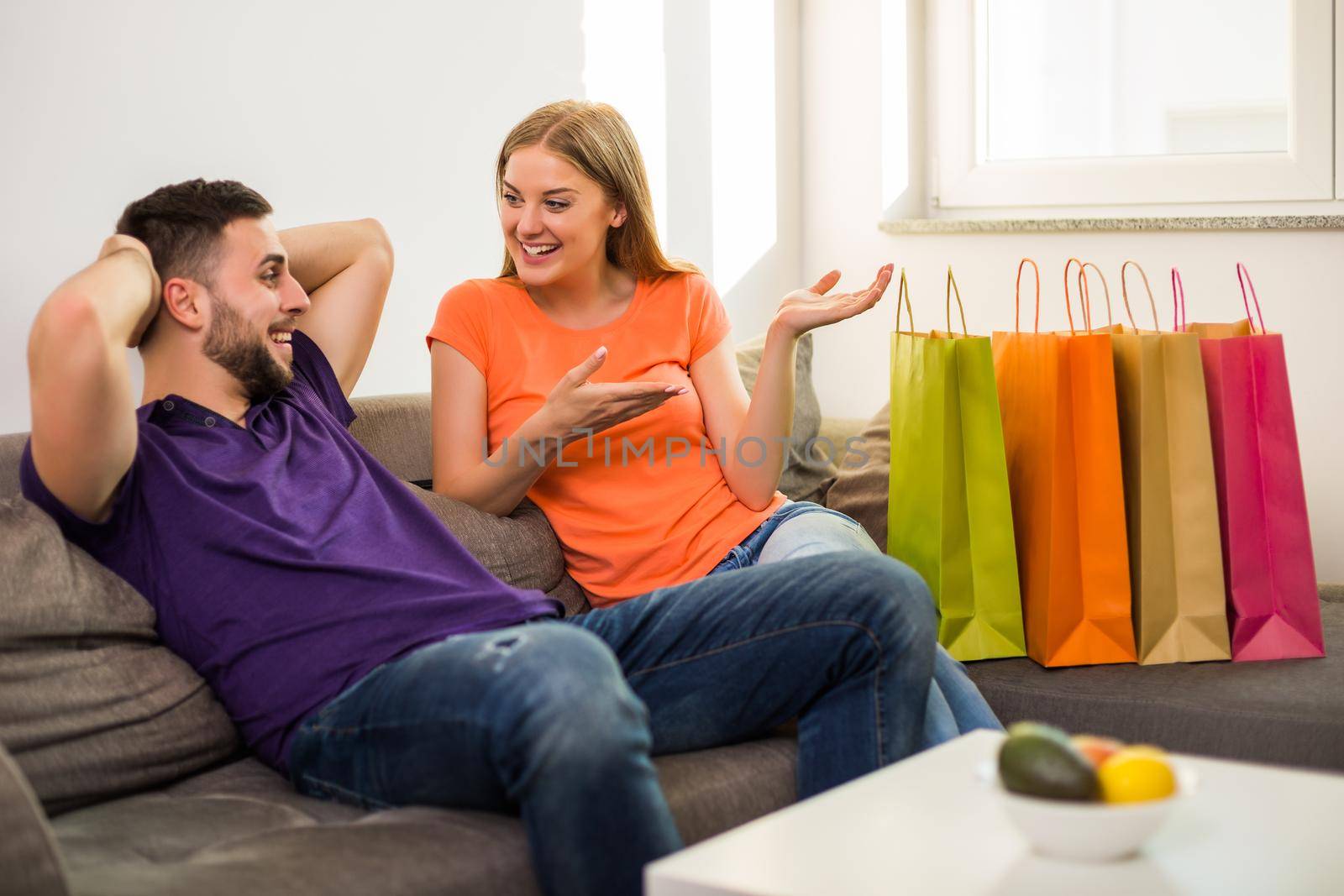 Wife is showing to her husband shopping bags while they sitting at their home.