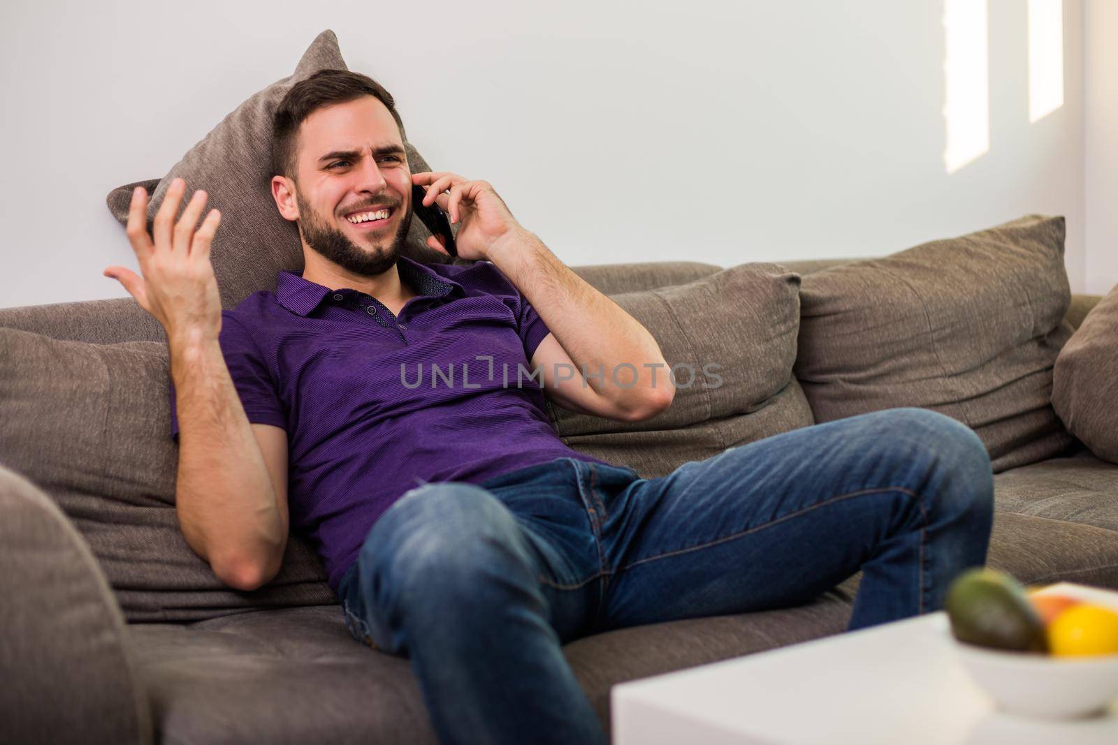 Young man man using mobile phone while sitting on sofa in his living room.