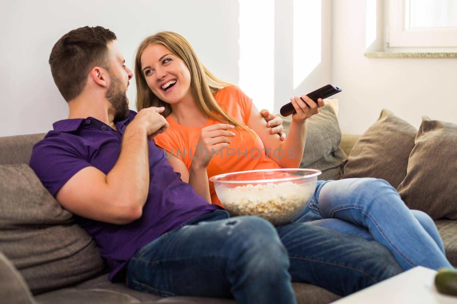 Happy couple enjoy watching tv, eating popcorn and spending time together at their home.