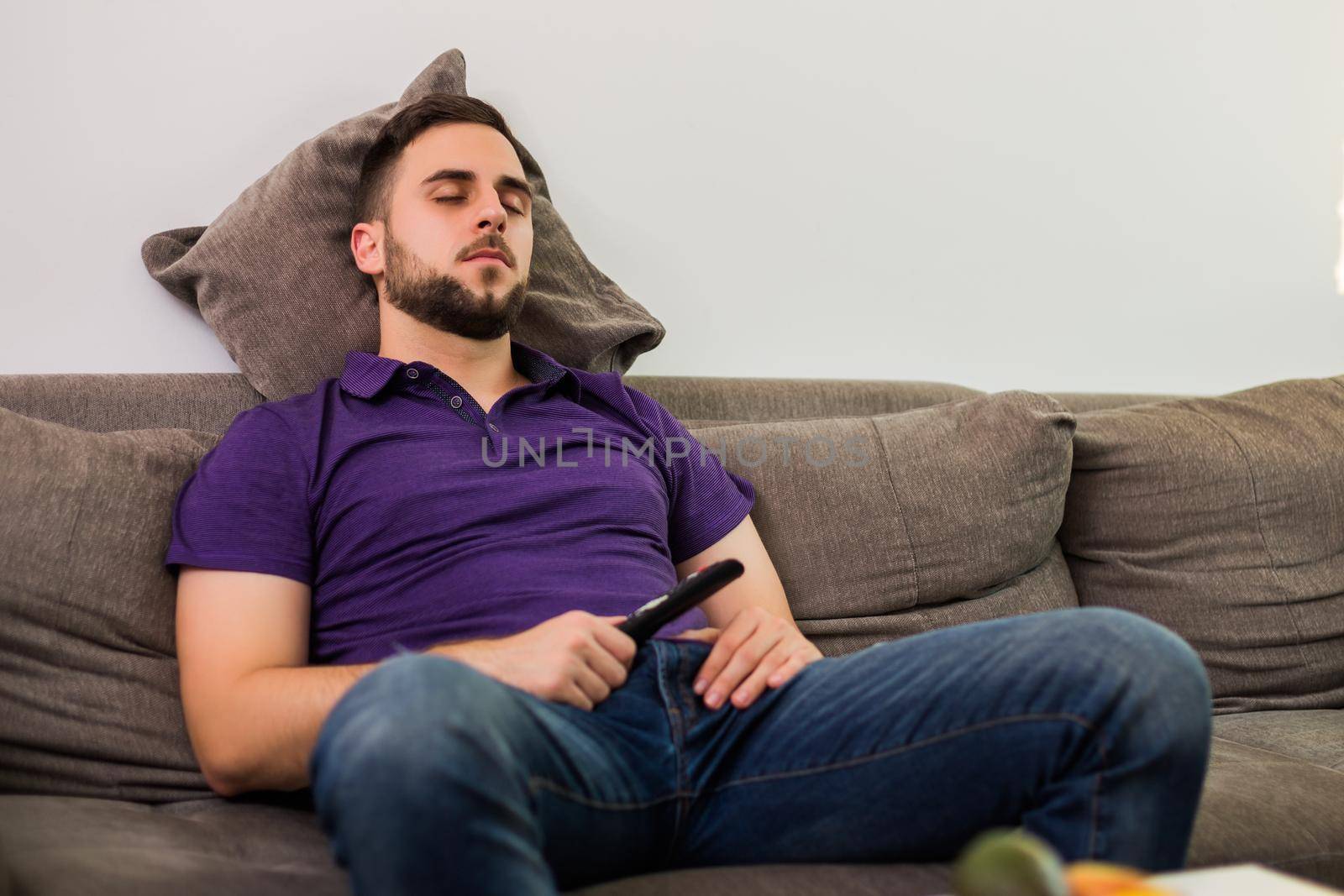 Man fell asleep while watching tv while sitting on sofa  in his living room.