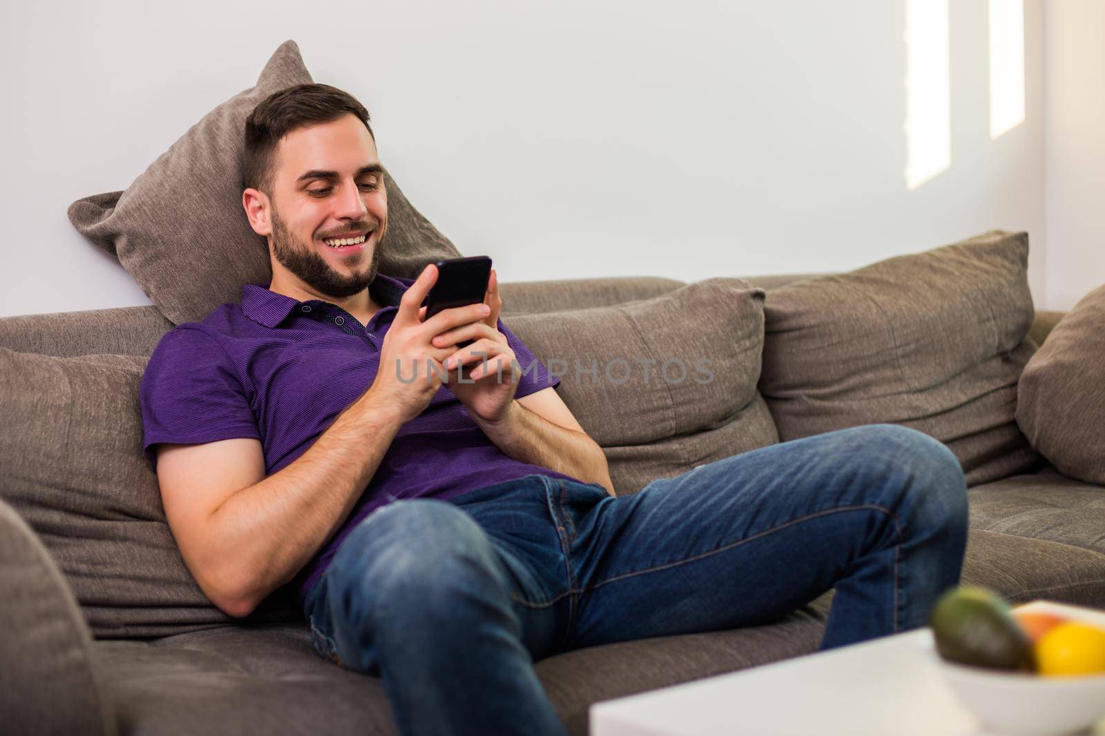 Young man man using mobile phone while sitting on sofa  in his living room.