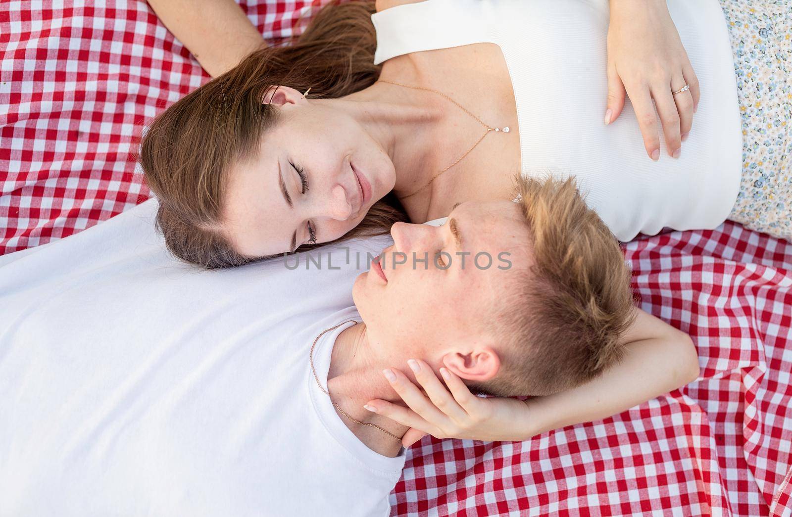 Young happy romantic couple cuddling on a picnic blanket looking to each other, top view