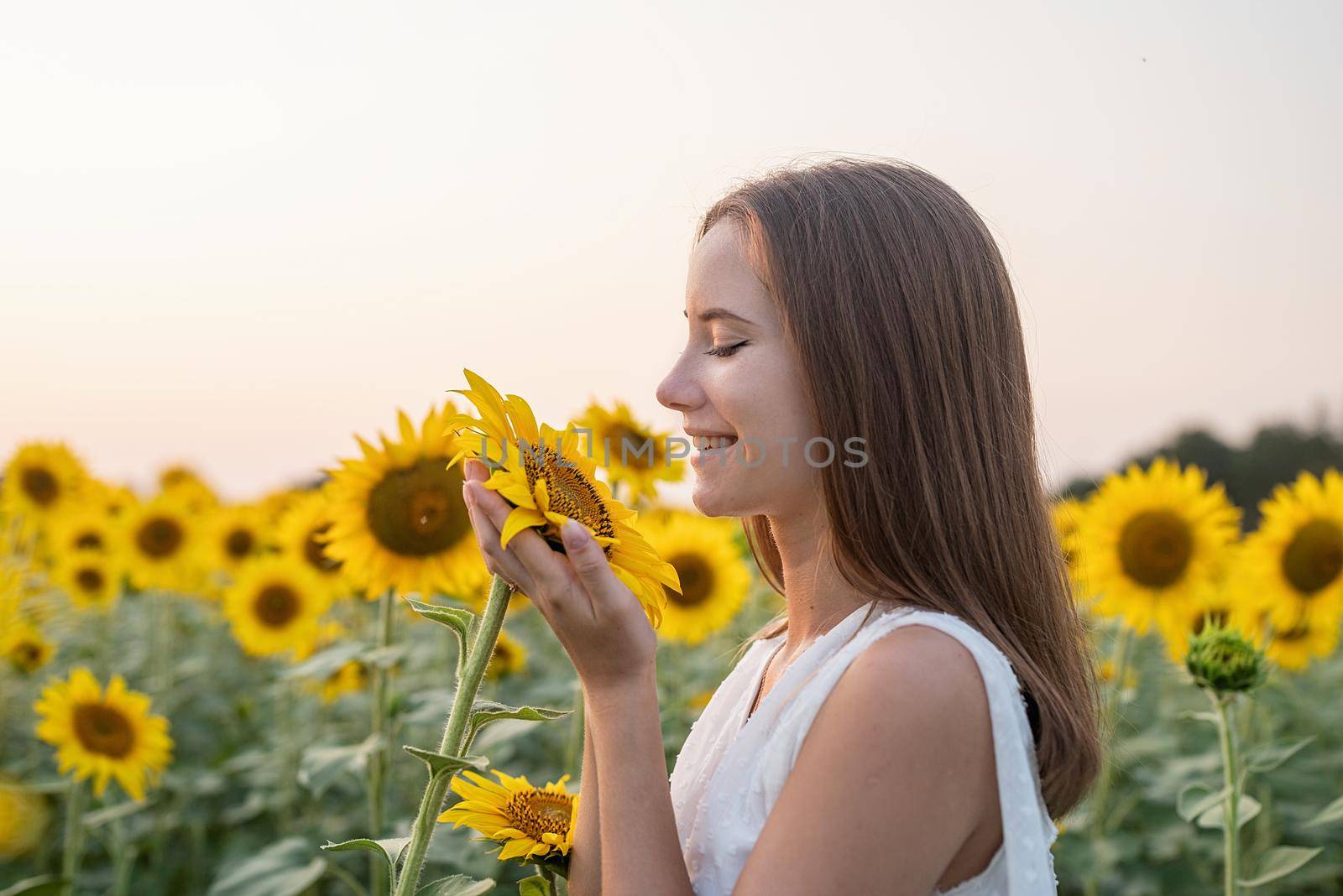 Freedom concept. Autumn nature. Girl in white dress smelling a sunflower blossom.