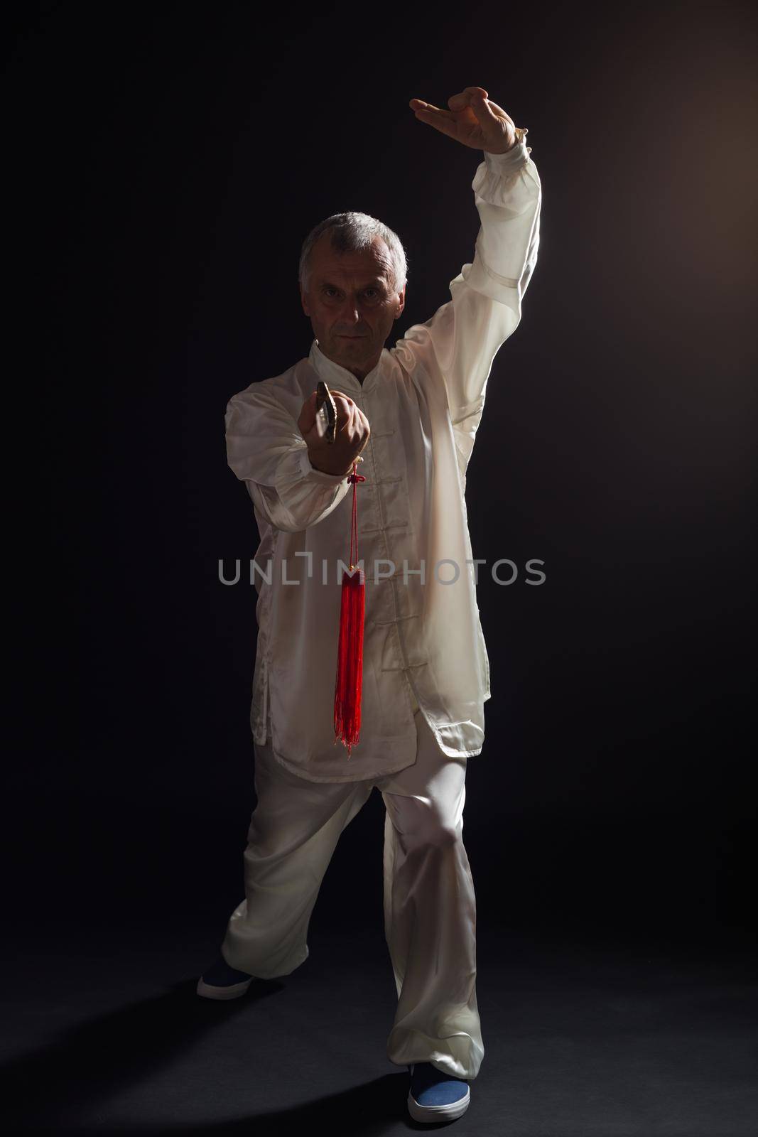 Senior man enjoys practicing Tai Chi with sword.