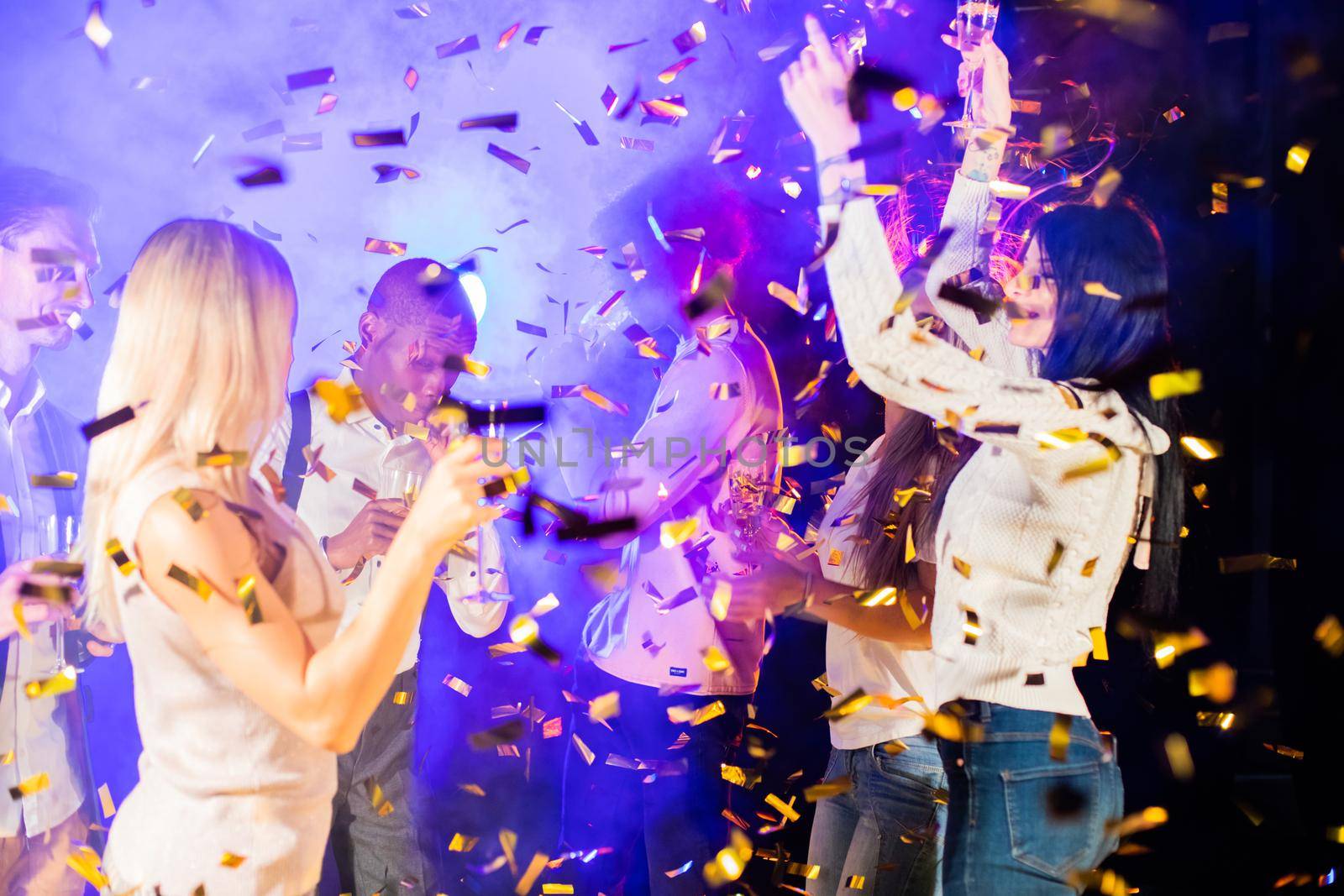 People dance at party in nightclub, drink champagne in falling confetti