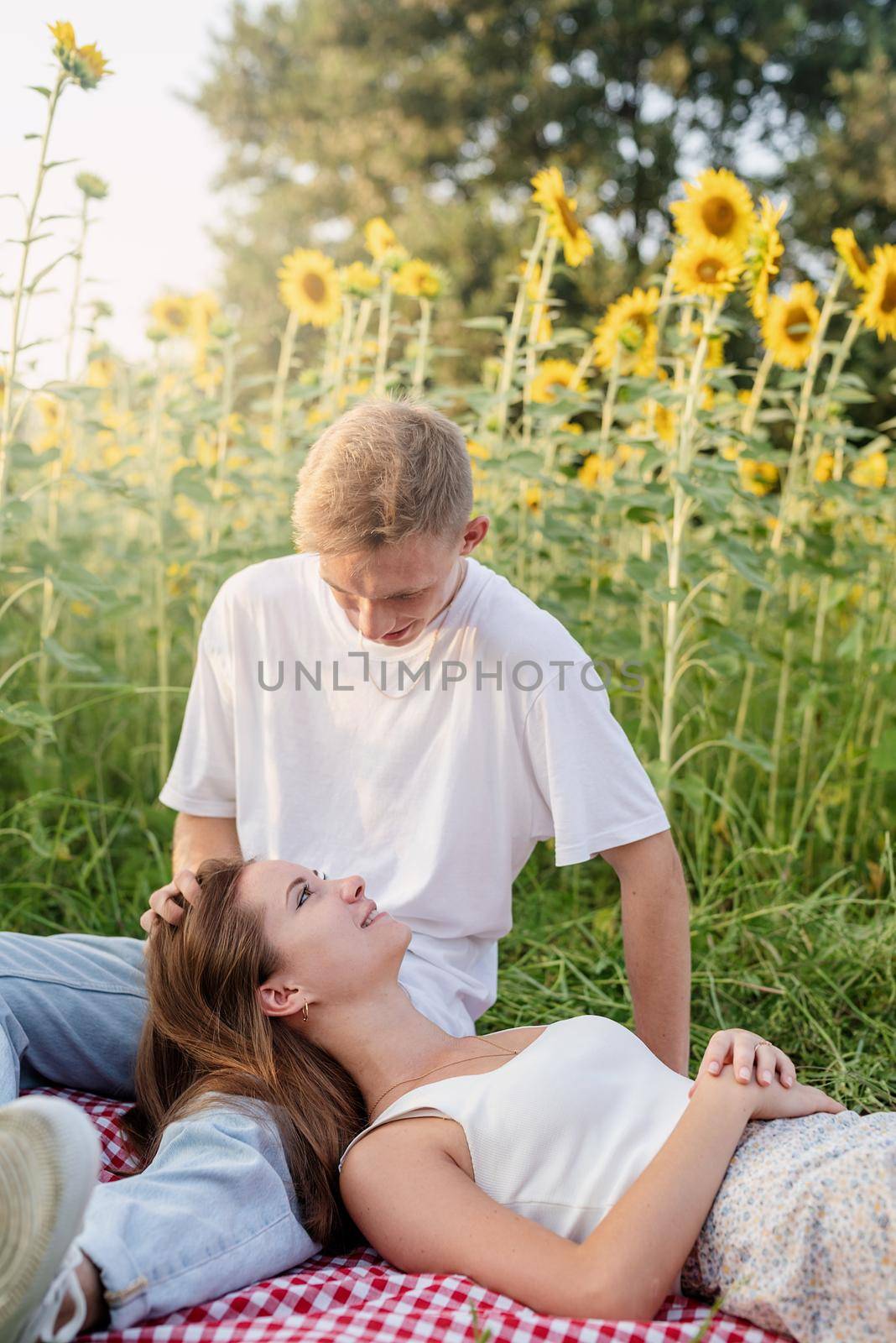 Autumn nature. Fun and liesure. Young teenage couple picnic on sunflower field in sunset, enjoying time together