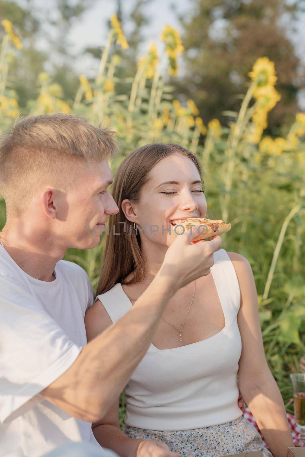 Autumn nature. Fun and liesure. Young teenage couple picnic on sunflower field in sunset eating pizza