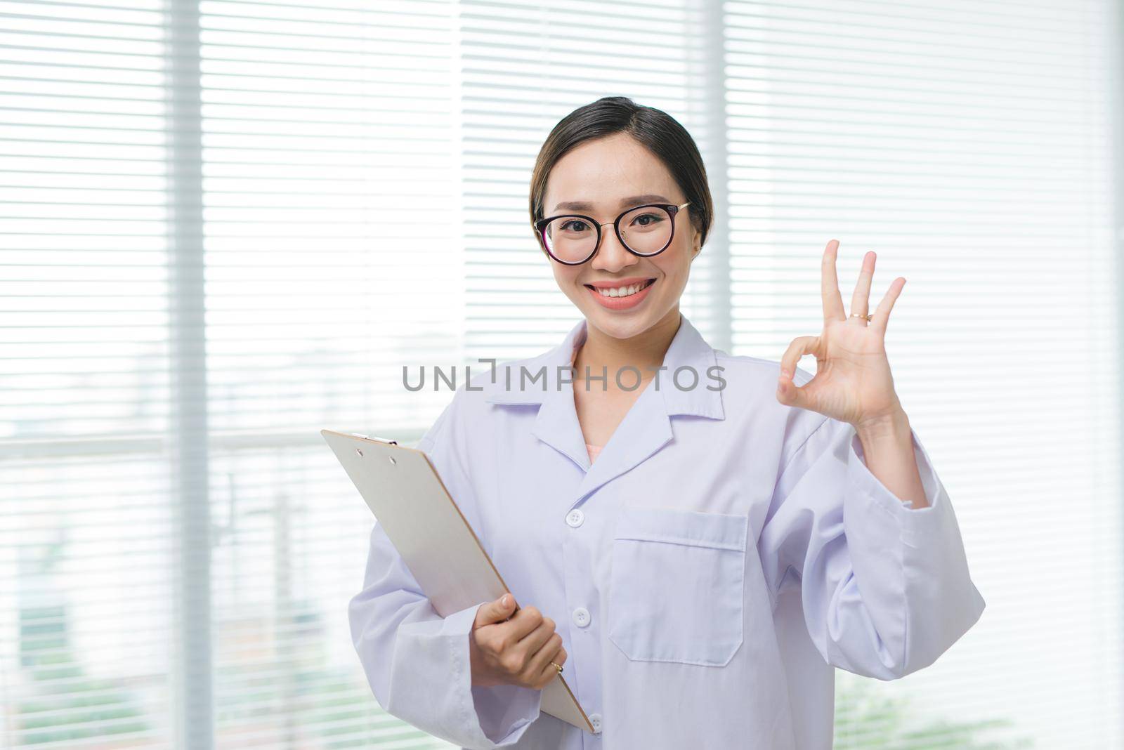 Young happy cheerful doctor in white uniform gesturing ok. Oral health care concept