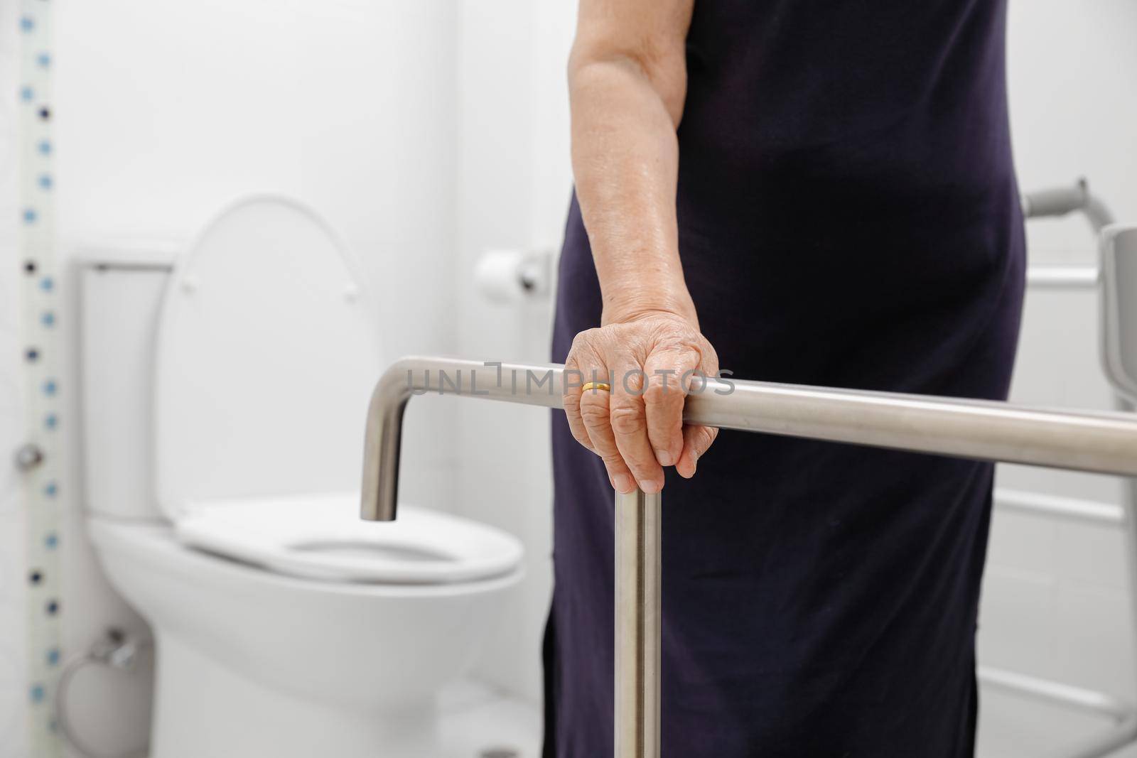 Elderly woman holding on handrail in toilet. by toa55