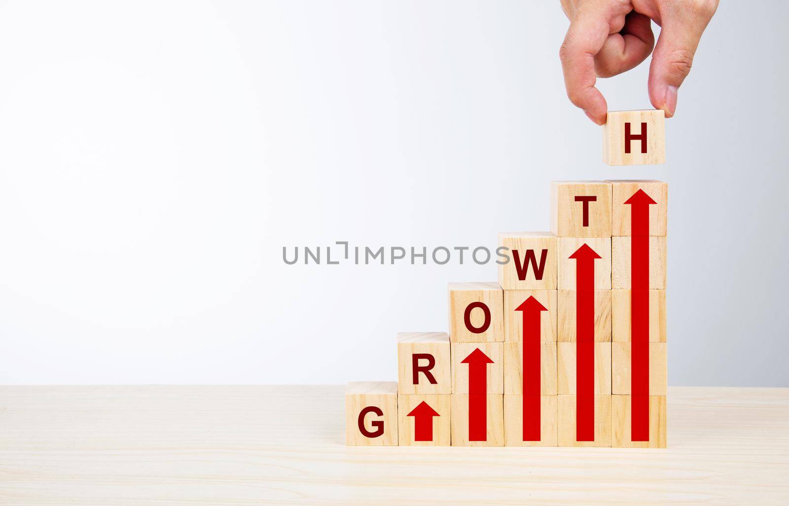 Hand arranging wood block stacking as step stair with arrow up and word GROWTH by tehcheesiong