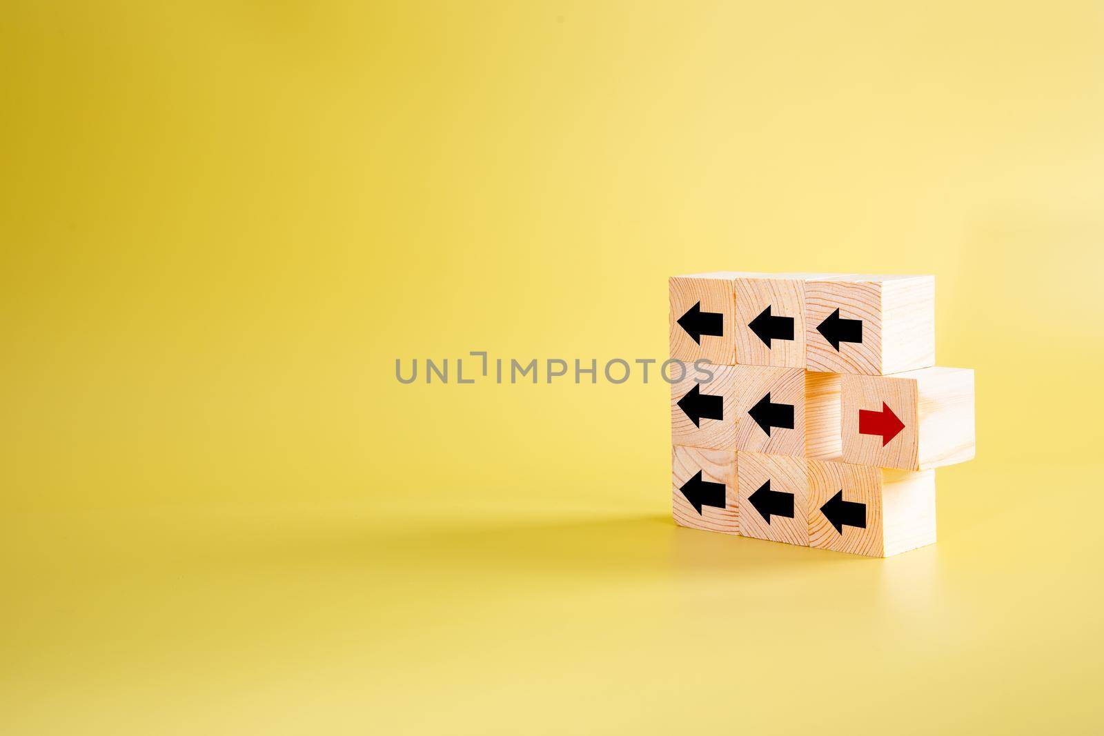 Wooden block with red arrow facing the opposite direction black arrows, think different and standing out from the crowd concept
