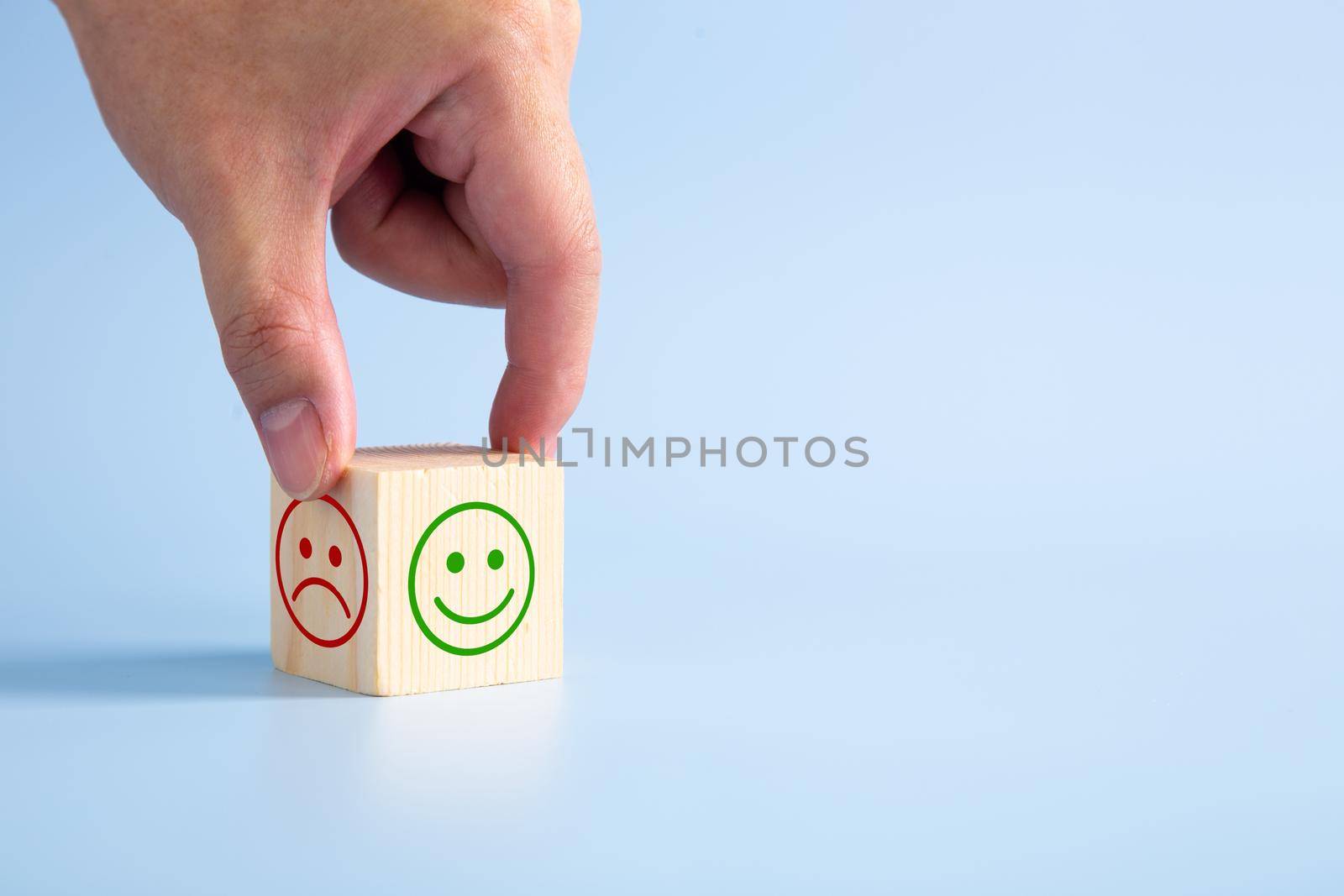 Hand turning a wooden block With Happy and Unhappy Face on blue background