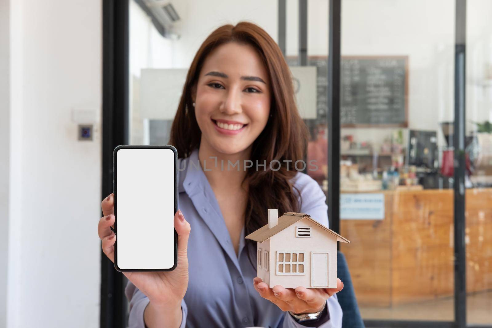 Real estate agent showing house model and mobile phone with blank white screen for advertisement by nateemee