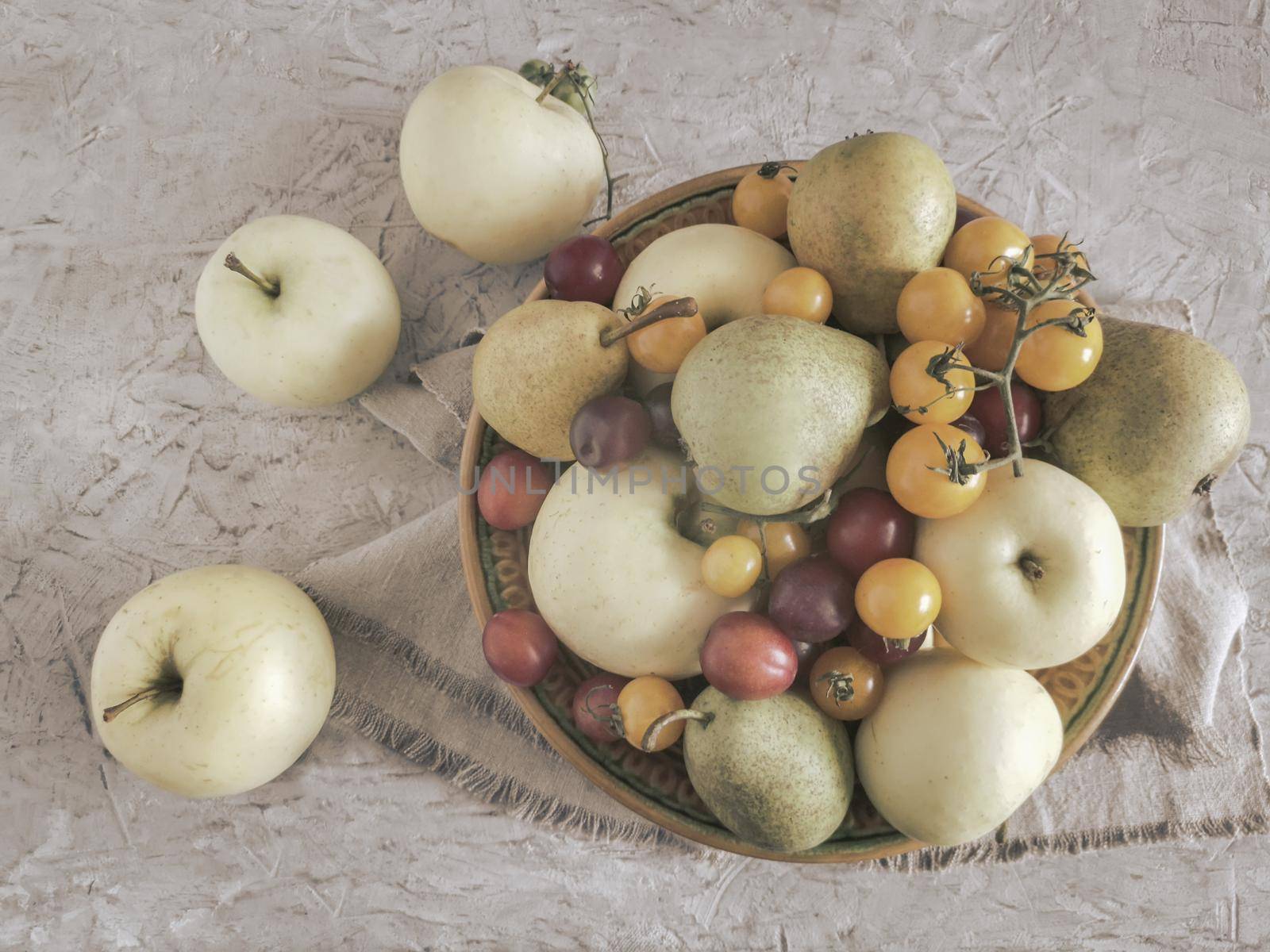 Ripe apples, pears and plums are on the table in a ceramic plate