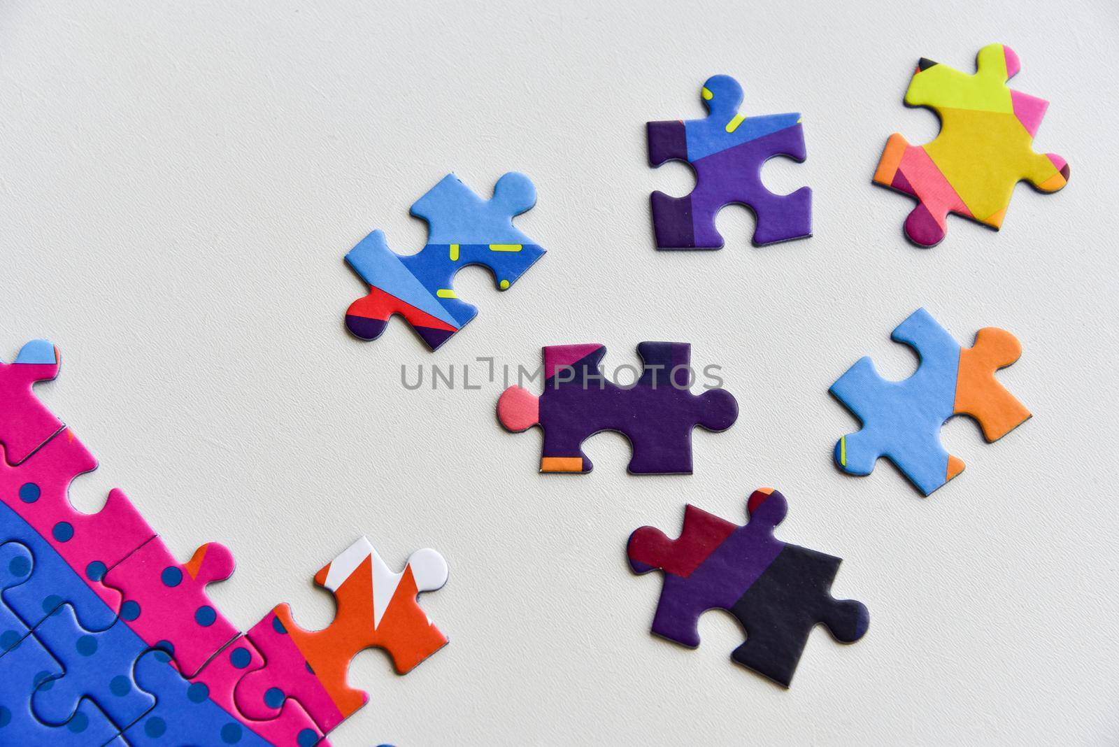 Fragment of a folded jigsaw puzzle and a pile of uncombed puzzle elements against the background of a white surface.