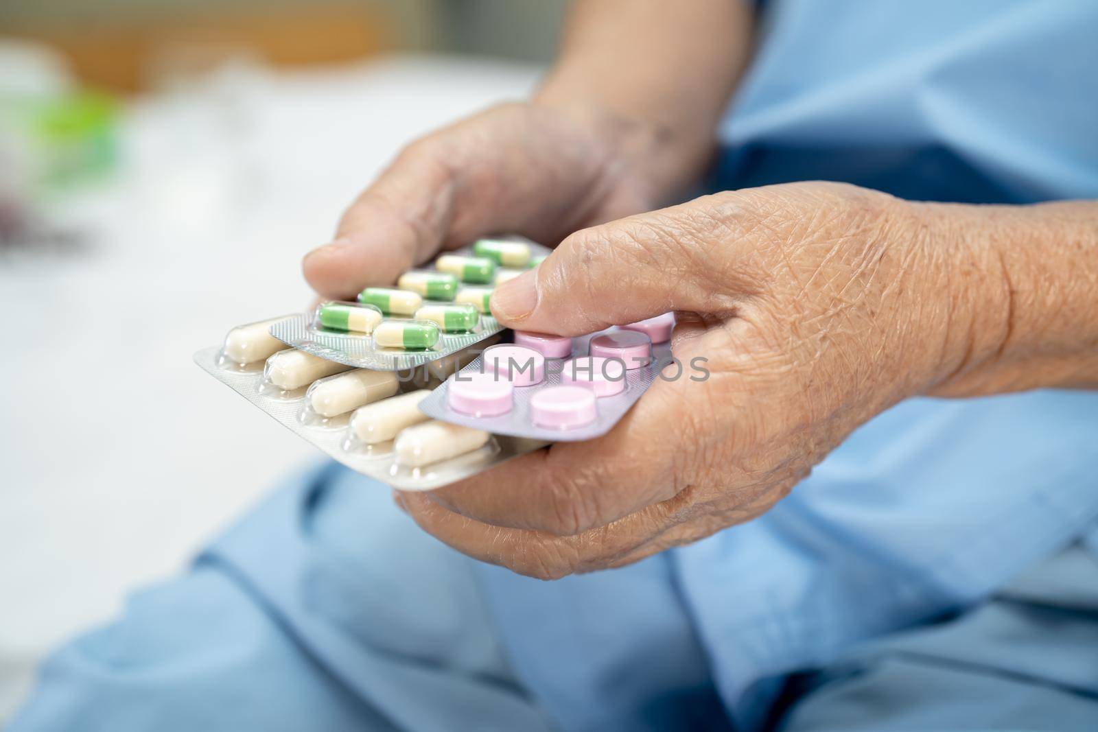 Asian senior or elderly old lady woman patient holding antibiotics capsule pills in blister packaging for treatment infection patient in hospital; Pharmacy drugstore concept.