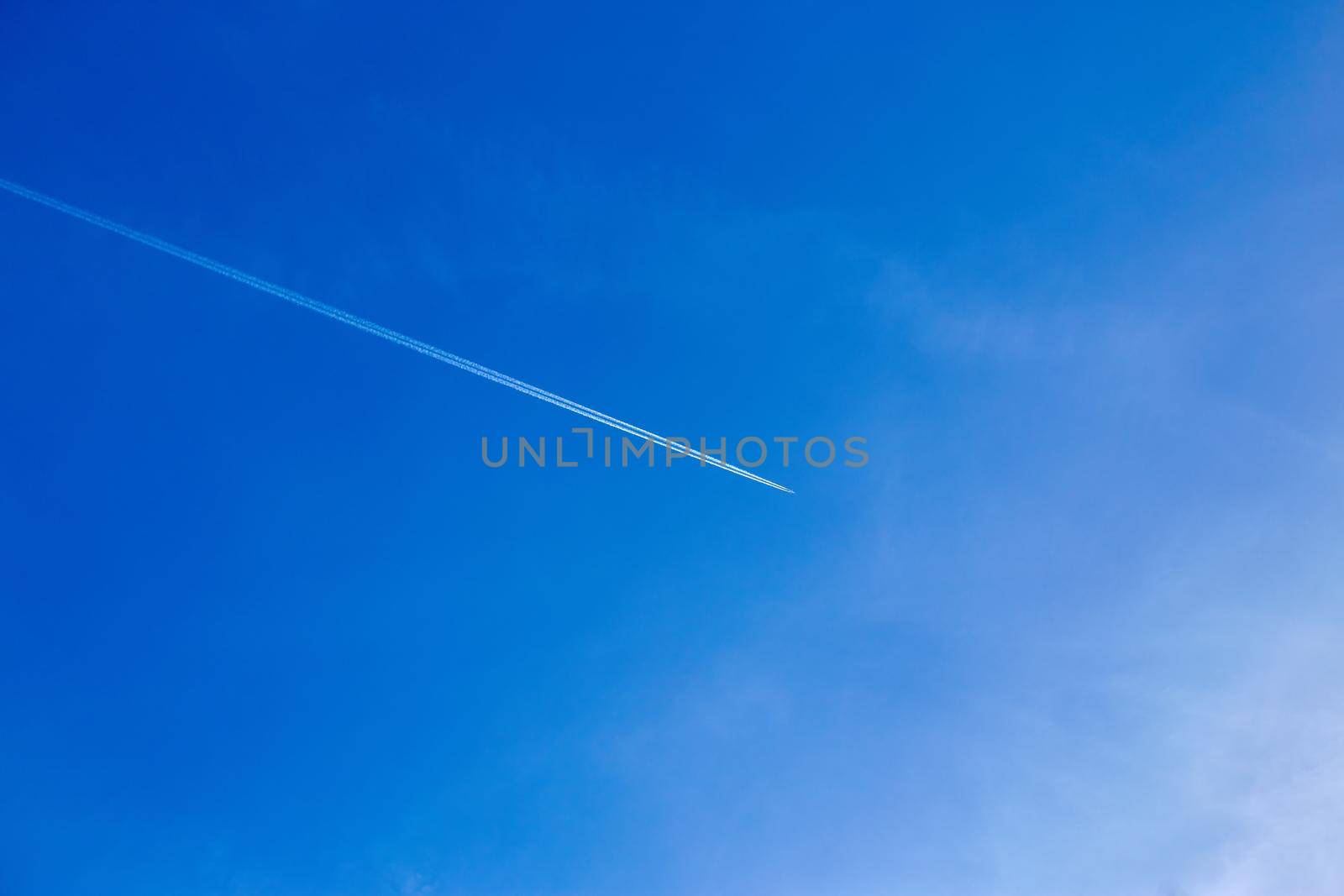 Airliner at high altitude with white condensation trails, on deep blue sky.