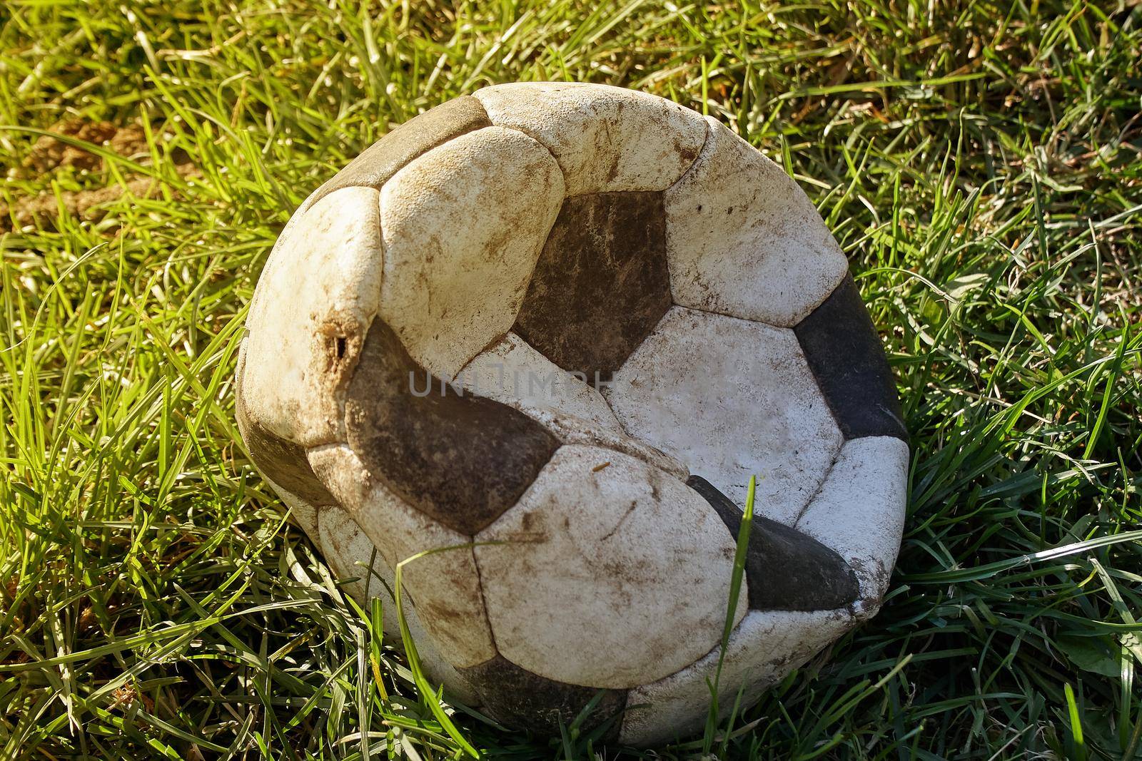 Torn football on the grass lawn. Soccer ball skin torn on the field