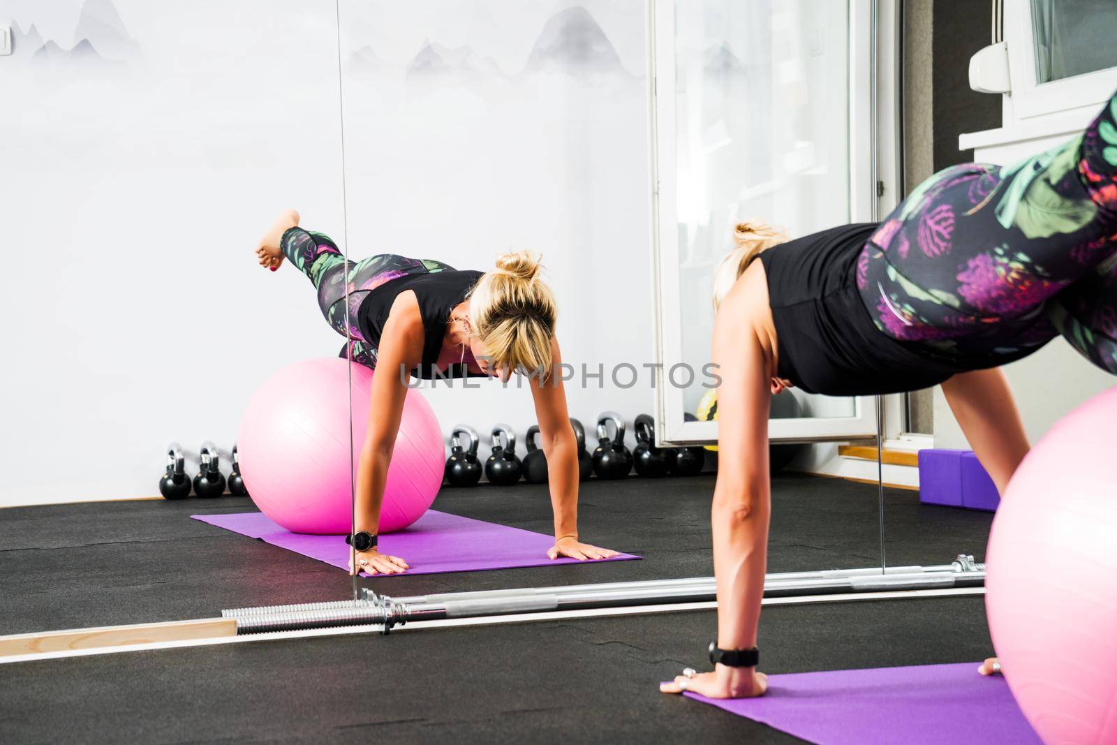 Adult woman is practicing pilates with ball in gym.