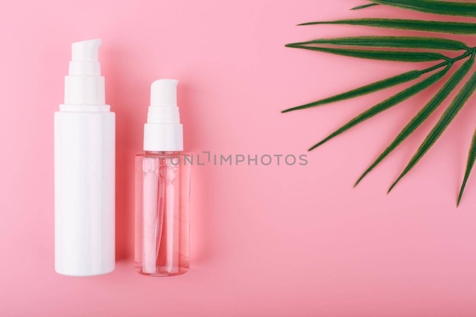 Set of cosmetic bottles for face cleansing, exfoliating and moisturizing against pink background with copy space and palm leaf. Trendy modern flat lay with a set of beauty products for daily use 