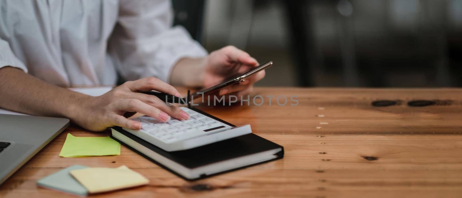 Close up hand of accounant or bookkeeper using calculator and mobile phone, calculating financial expense at home office.