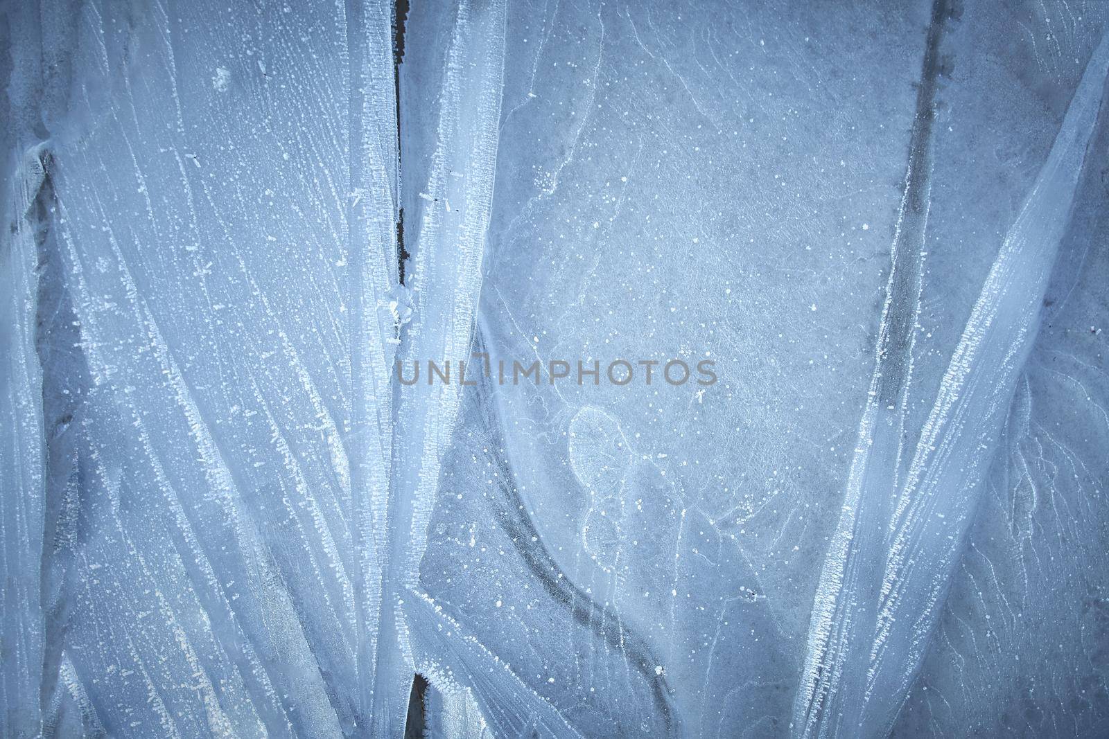 The surface of natural ice covering the puddle in late autumn. Ice texture with intersperses of white frost, crystals of frozen water. Rime.