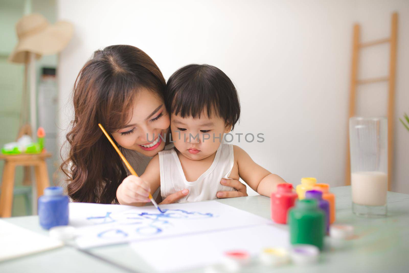 Happy family mother and daughter together paint. Asian woman helps her child girl.