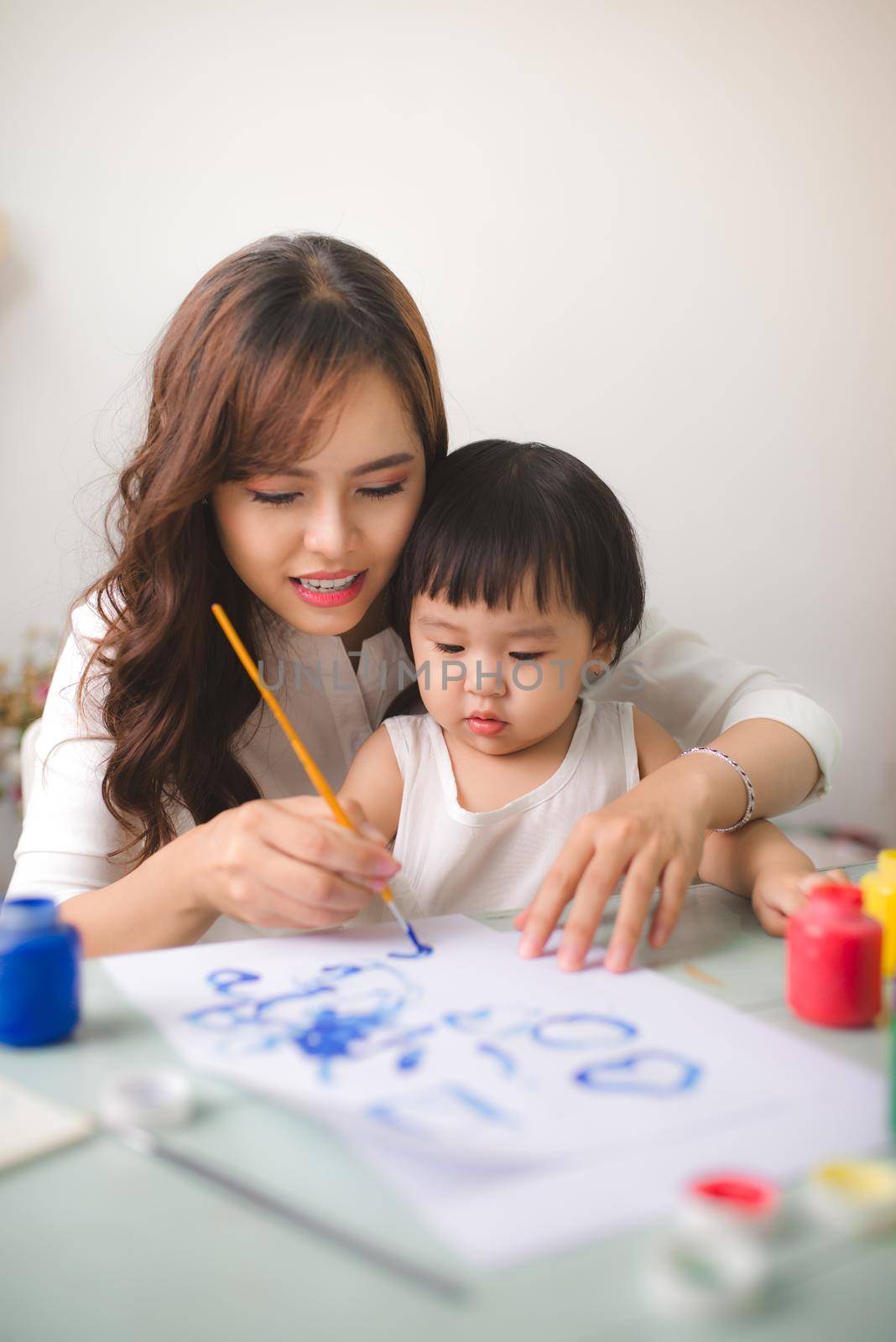 Happy family mother and daughter together paint. Asian woman helps her child girl.