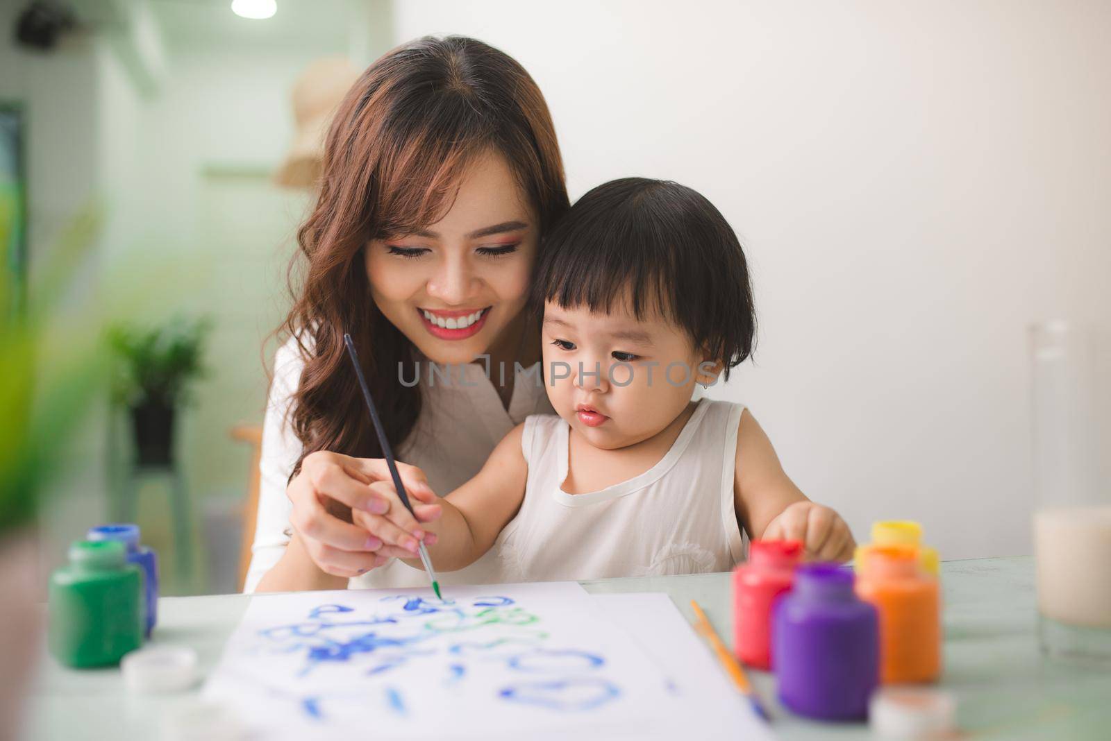 Happy family mother and daughter together paint. Asian woman helps her child girl. by makidotvn